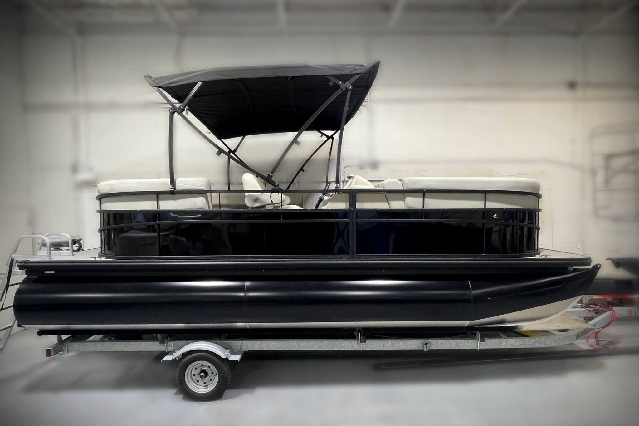 The 2024 WX Tritoon WX-003 shown on a trailer indoors, highlighting its triple-tube tritoon hull design and overall size suited for stable, spacious cruising.