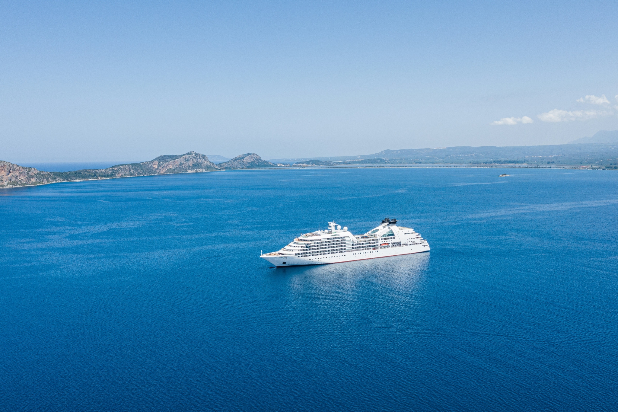 A boutique cruise ship sailing along a clear, blue coastline, exemplifying the rise of intimate, small-ship experiences in 2025 Cruise Trends.
