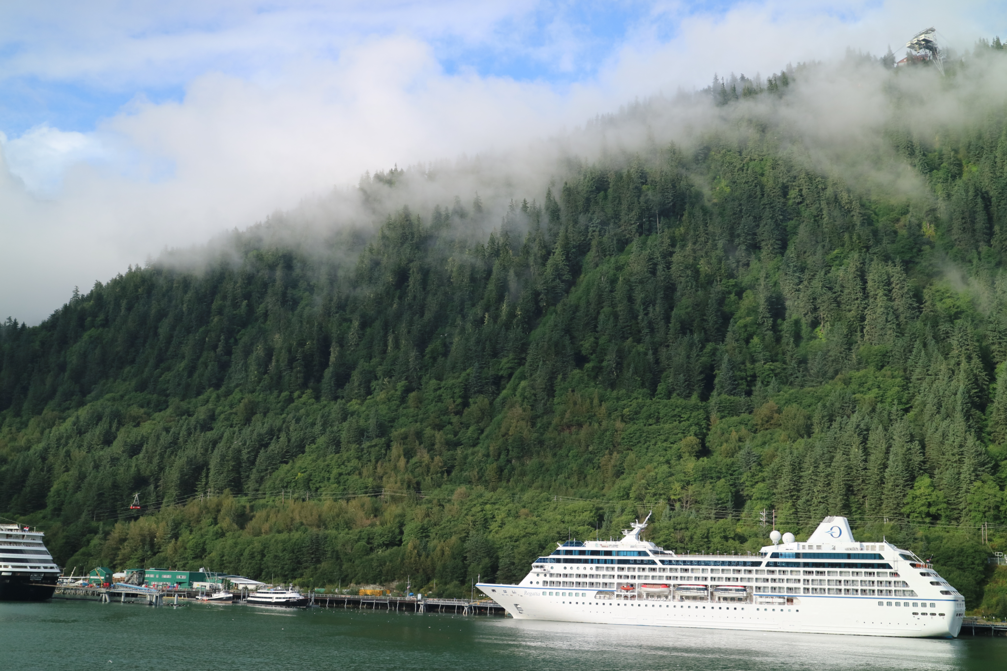 A serene cruise ship docked at a scenic port surrounded by forested mountains, representing eco-conscious itineraries popular in 2025 Cruise Trends.