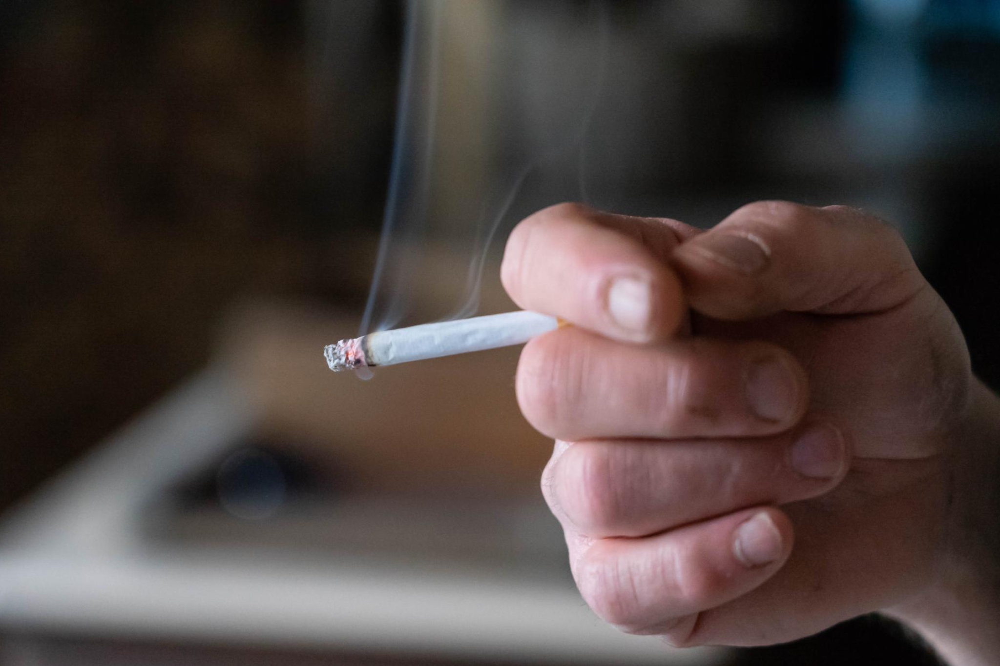 A person holding a lit cigarette indoors, depicting things you should never do in your cruise cabin, including smoking or vaping in prohibited areas.