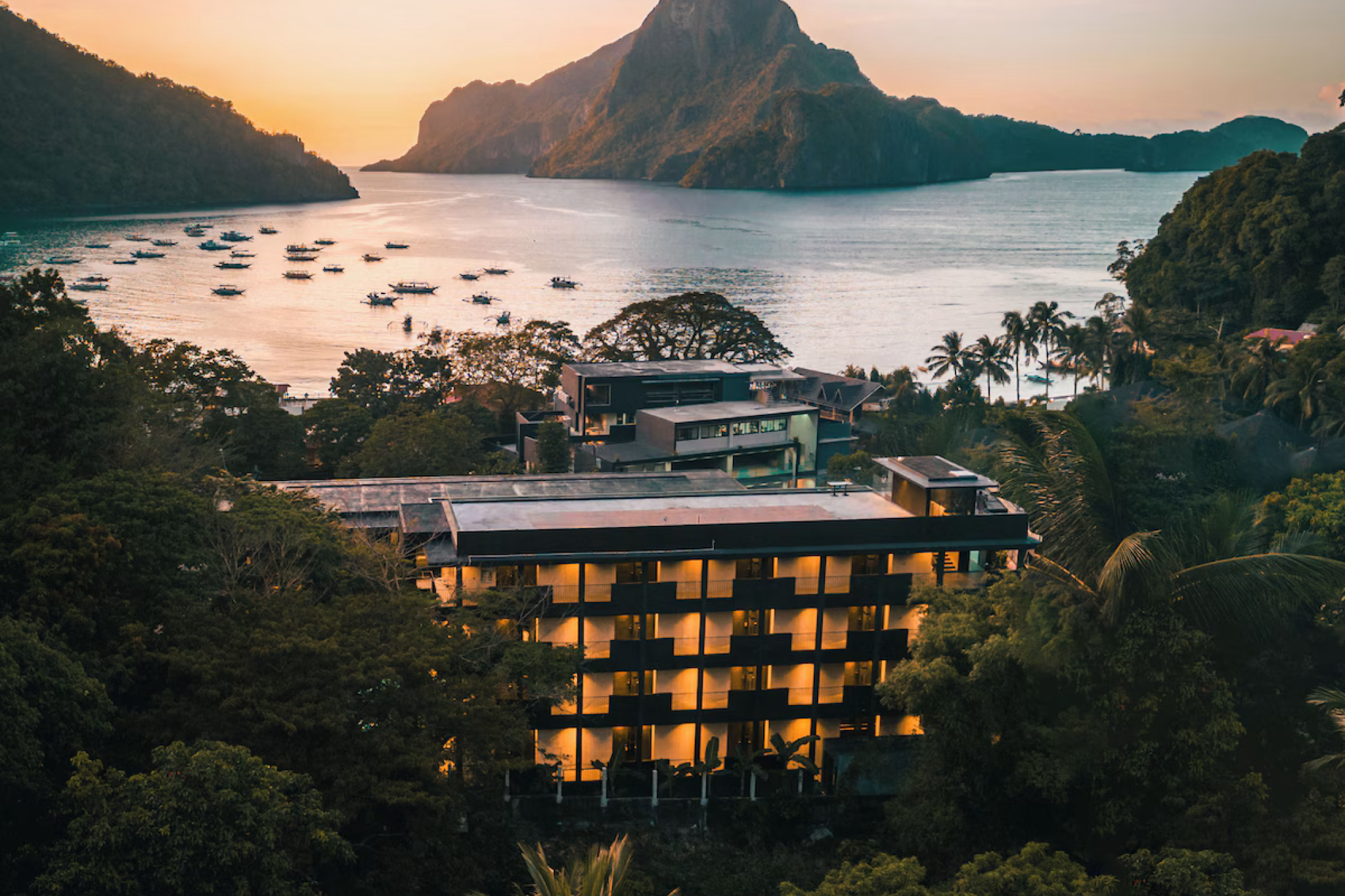 Elevated view of The Funny Lion El Nido resort with warm-lit rooms overlooking Bacuit Bay and dramatic limestone cliffs — the top-rated choice among the best beach resorts in El Nido Palawan for 2025.