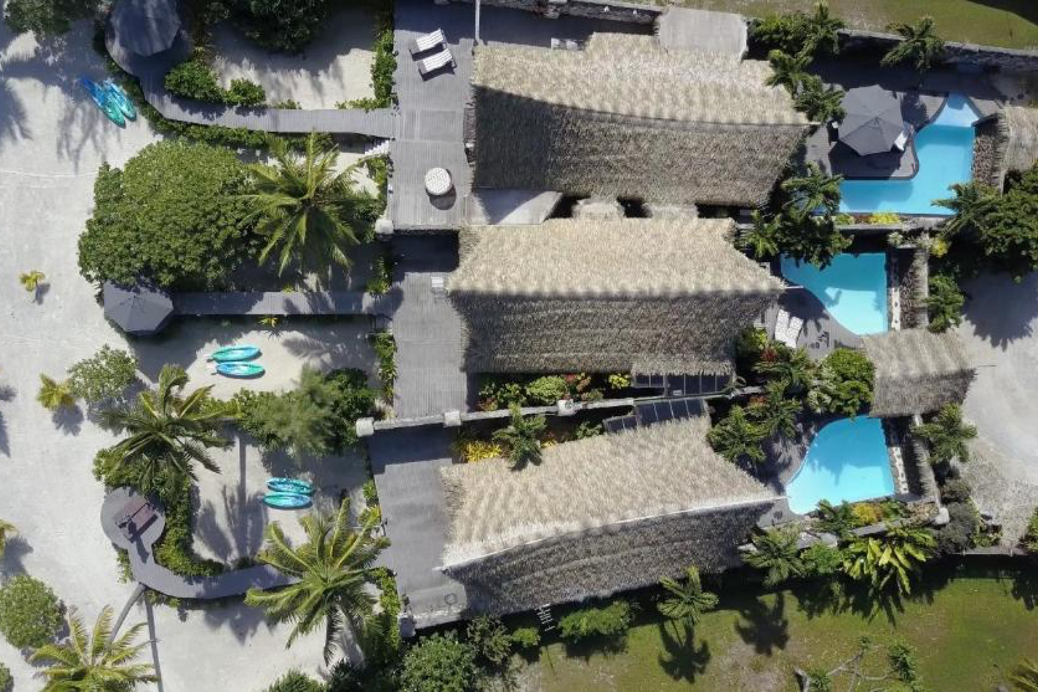 Aerial view of Aitutaki Escape’s three private villas with thatched roofs and turquoise plunge pools surrounded by palm gardens, one of the best Aitutaki resorts for secluded luxury.