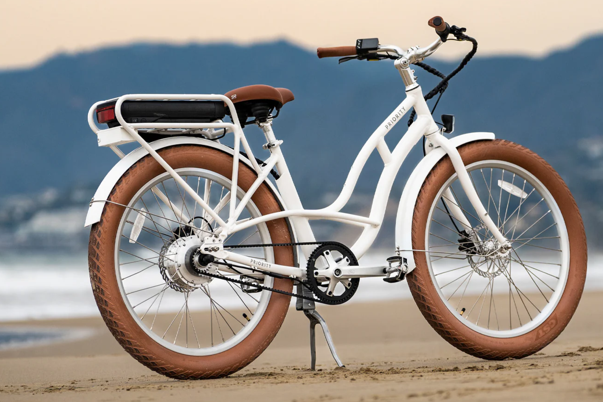 Priority Coast electric beach cruiser with rust-resistant frame and wide brown tires parked on sandy beach — one of the best beach cruisers for durability and coastal performance.