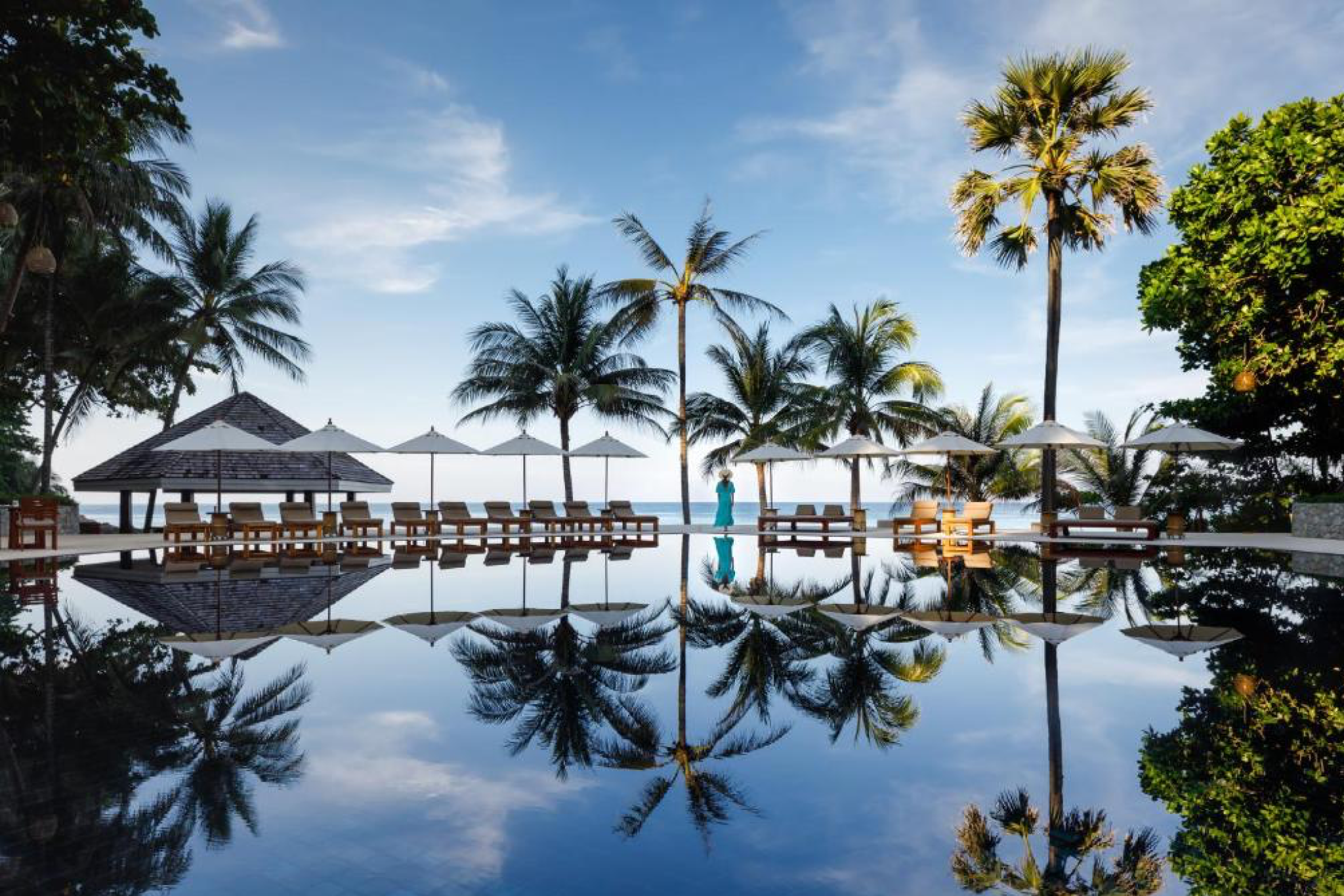 Seaside infinity pool framed by palm trees at The Surin Phuket, offering privacy and elegance
