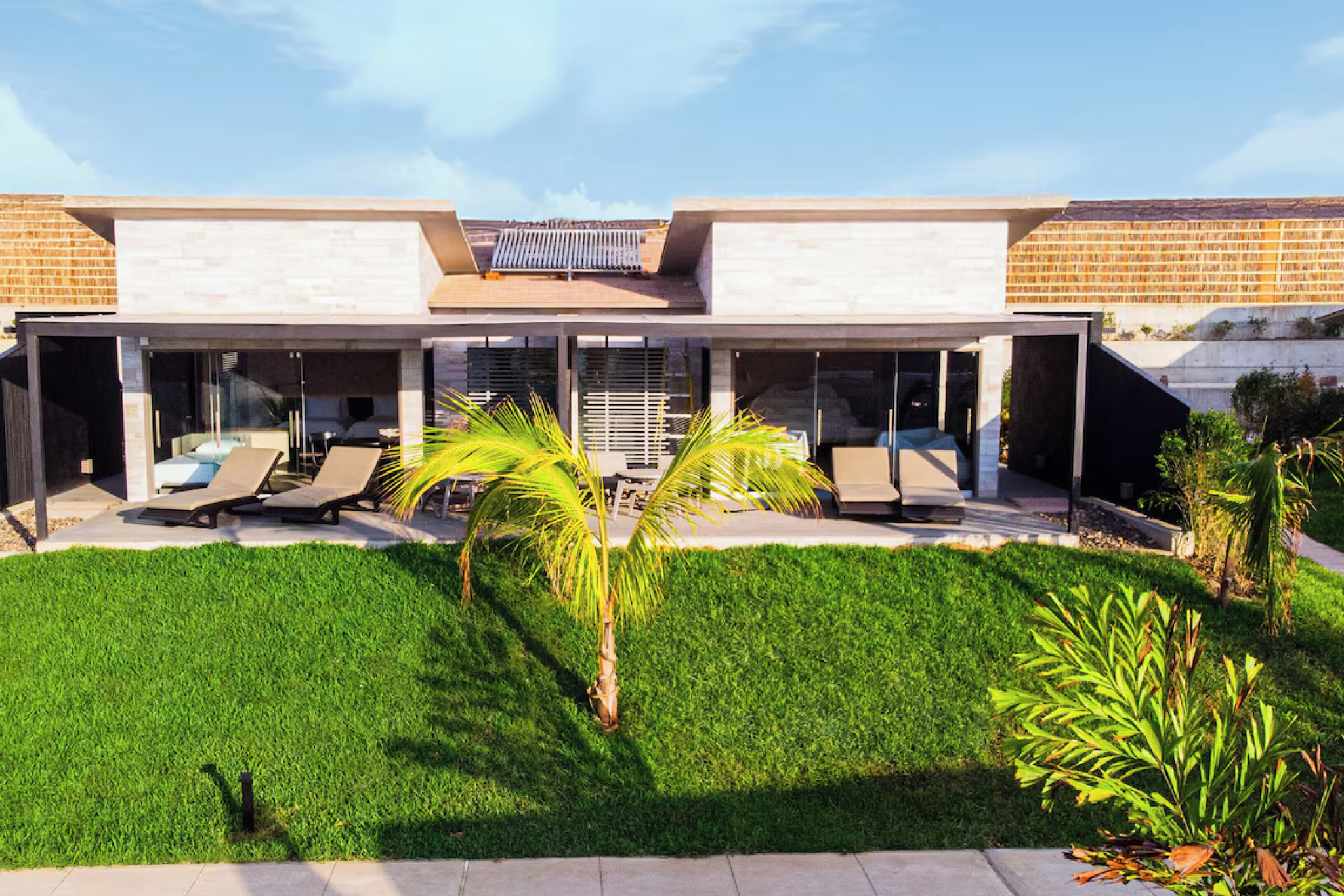 A sunlit exterior of Arennas Mancora with modern low-rise villas, wide glass doors, manicured lawns, and a small palm tree framing the clean architectural style — capturing the contemporary coastal luxury that places it among the best beach resorts in South America in 2025.