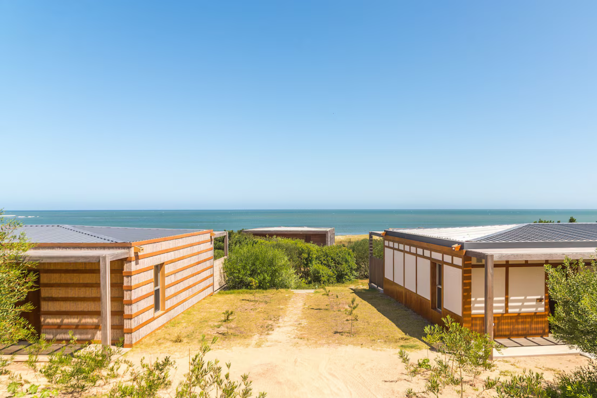 A bright daytime shot of Bahía Vik José Ignacio’s ocean-facing bungalows framed by dunes and greenery, showcasing contemporary lines and natural textures overlooking a wide, tranquil Atlantic shoreline — a defining feature of one of the best beach resorts in South America in 2025.