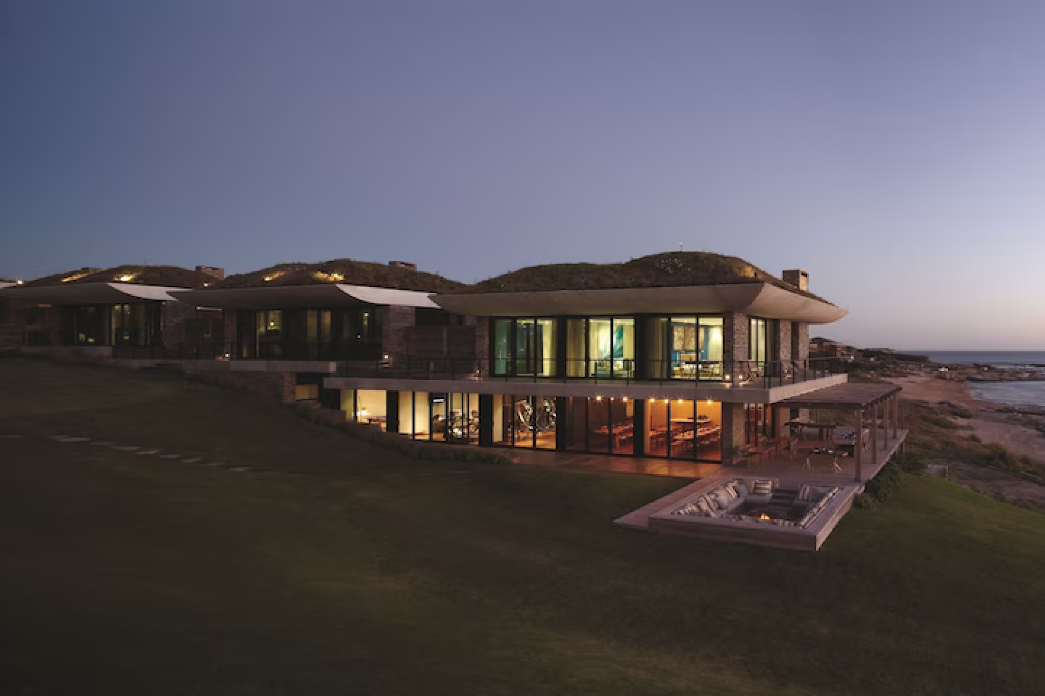 A dusk view of Playa Vik José Ignacio’s striking titanium-and-glass architecture, featuring curved rooflines, expansive windows, and a multi-level design overlooking the Atlantic — a bold artistic landmark recognized as one of the best beach resorts in South America in 2025.