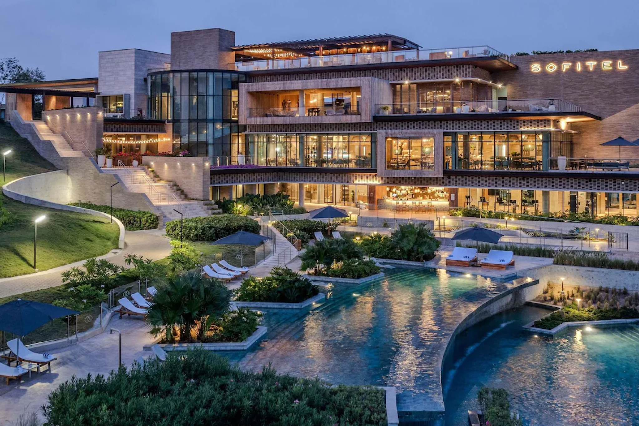 A vibrant evening view of Sofitel Barú Calablanca’s terraced architecture glowing with warm lights above expansive lagoon-style pools, surrounded by lush tropical landscaping — illustrating the refined Caribbean elegance that secures its place among the best beach resorts in South America in 2025.
