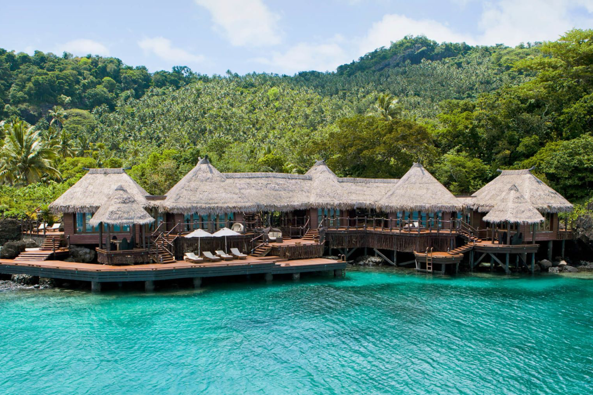 Secluded beachfront villas and lush hills of Laucala Island overlooking a wide lagoon, showcasing its ultra-luxury environment as one of the best beach resorts in the South Pacific in 2025.