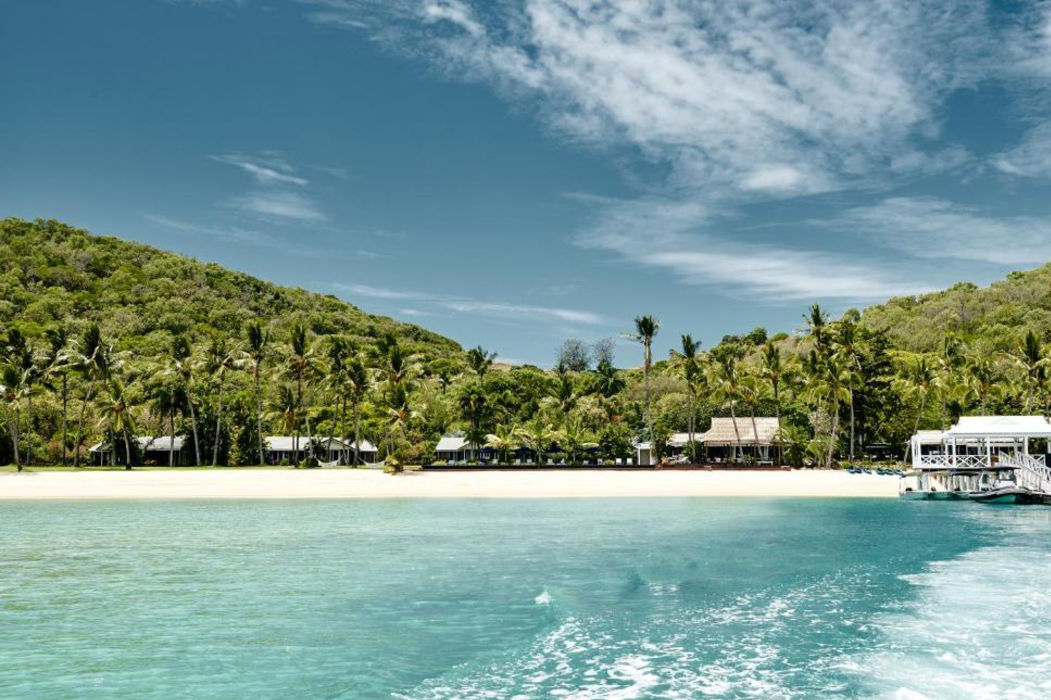 Orpheus Island Lodge shoreline captured from the water, showcasing palm-lined beaches, lush green hills, and calm turquoise seas — a defining scene from one of the best beach resorts in the South Pacific in 2025.