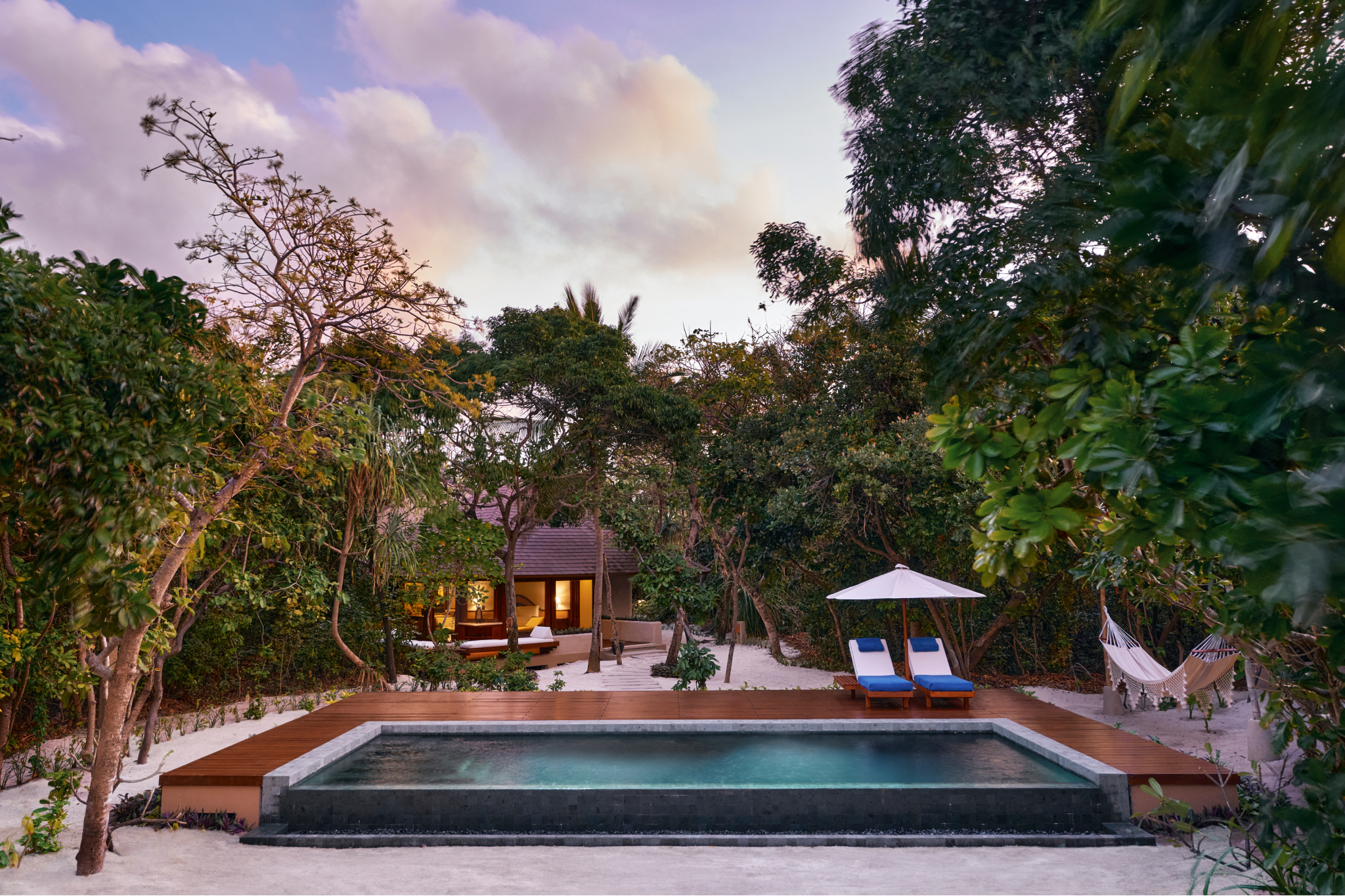A serene beachfront villa at Amanpulo, ranked #1 among the best beach resorts in Southeast Asia in 2025, featuring a private pool, shaded loungers, white sandy pathways, and lush vegetation under a soft sunset sky.