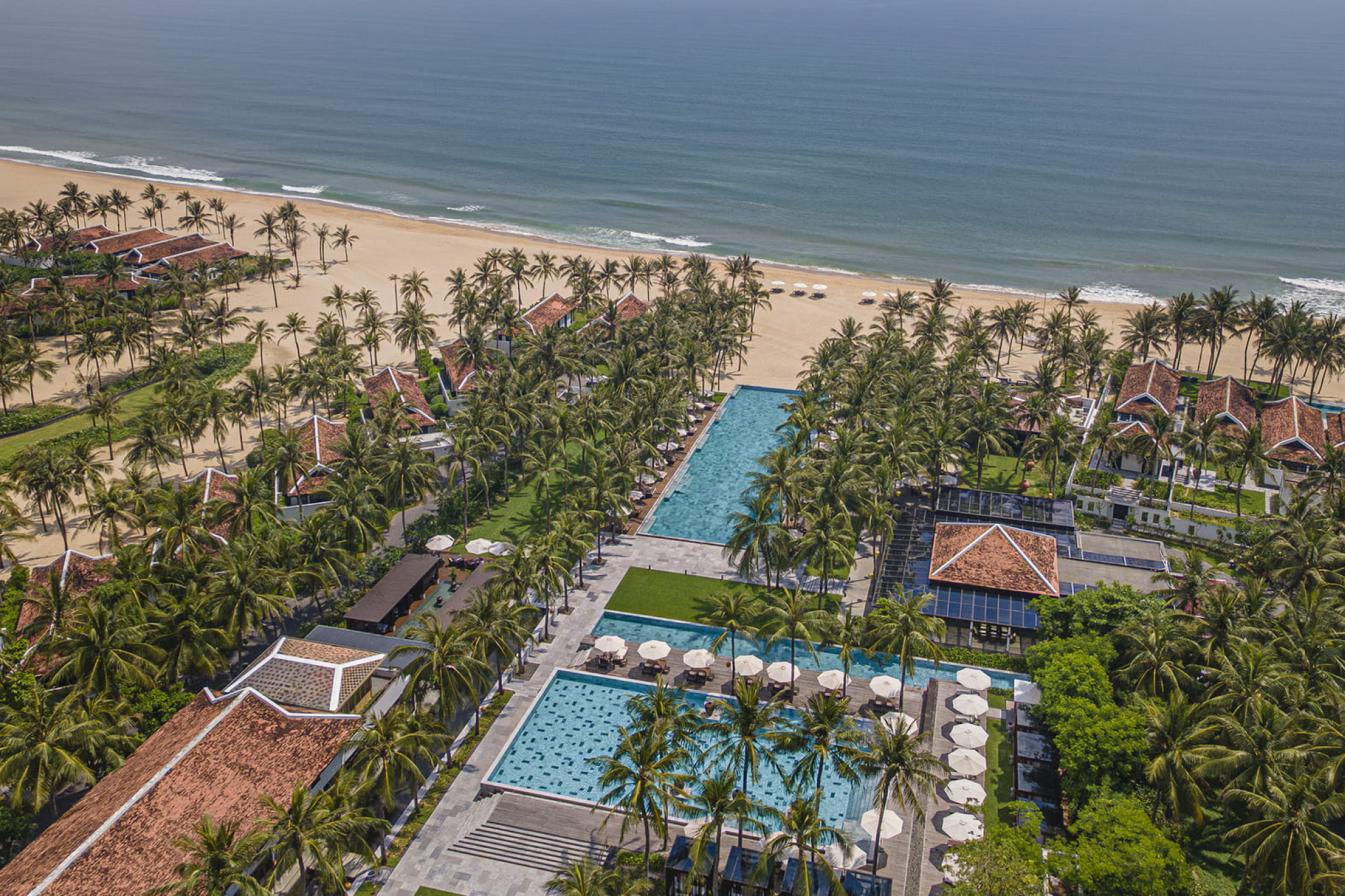 An aerial beachfront panorama of Four Seasons Resort The Nam Hai, one of the best beach resorts in Southeast Asia in 2025, showing long palm-lined pools, beachfront villas, and the golden sands of Ha My Beach stretching along the Vietnamese coastline.