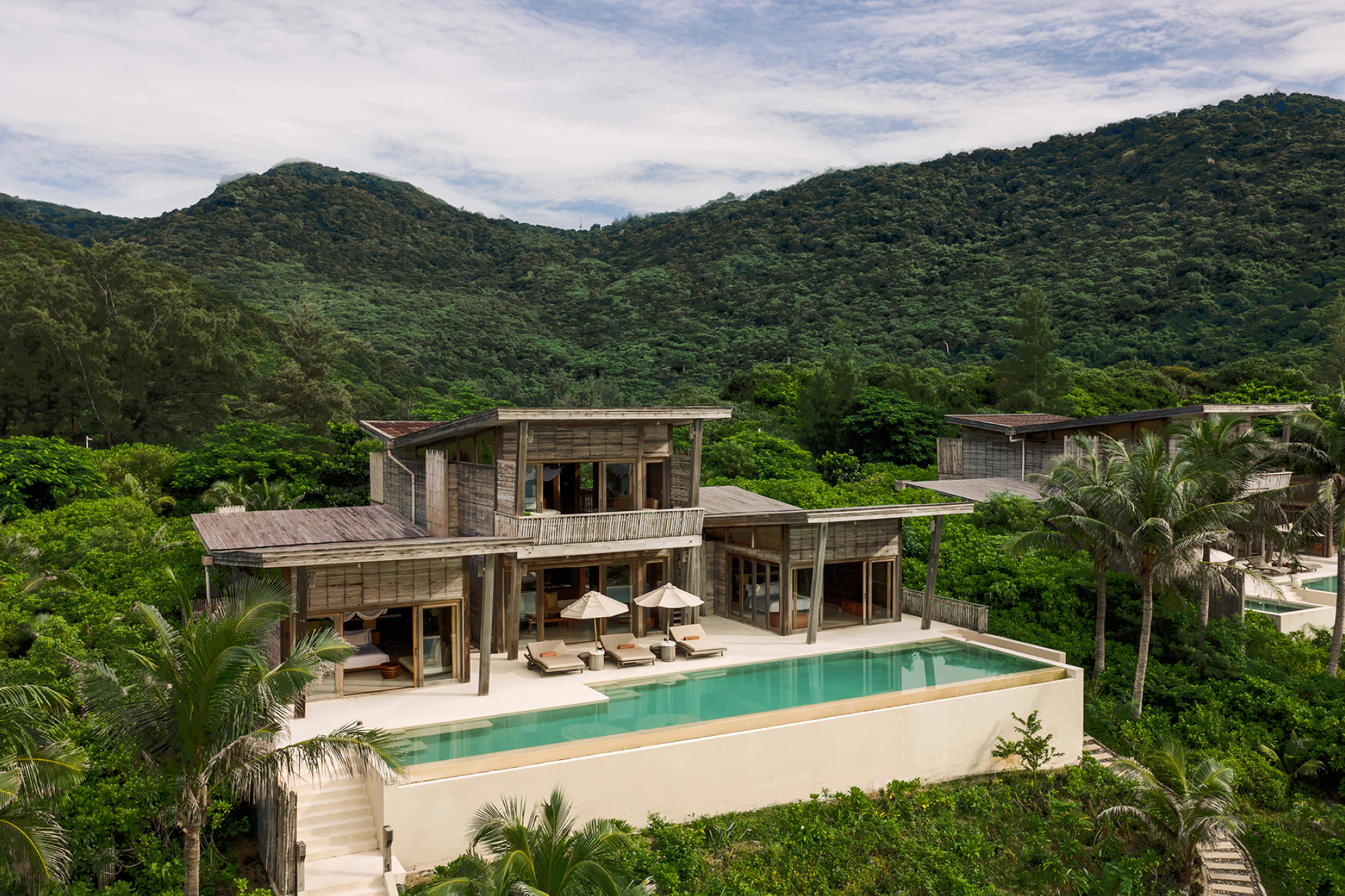 A serene villa-side view of Six Senses Con Dao, recognized as one of the best beach resorts in Southeast Asia in 2025, featuring minimalist wooden architecture, a private infinity pool, and lush green mountains forming a dramatic natural backdrop.