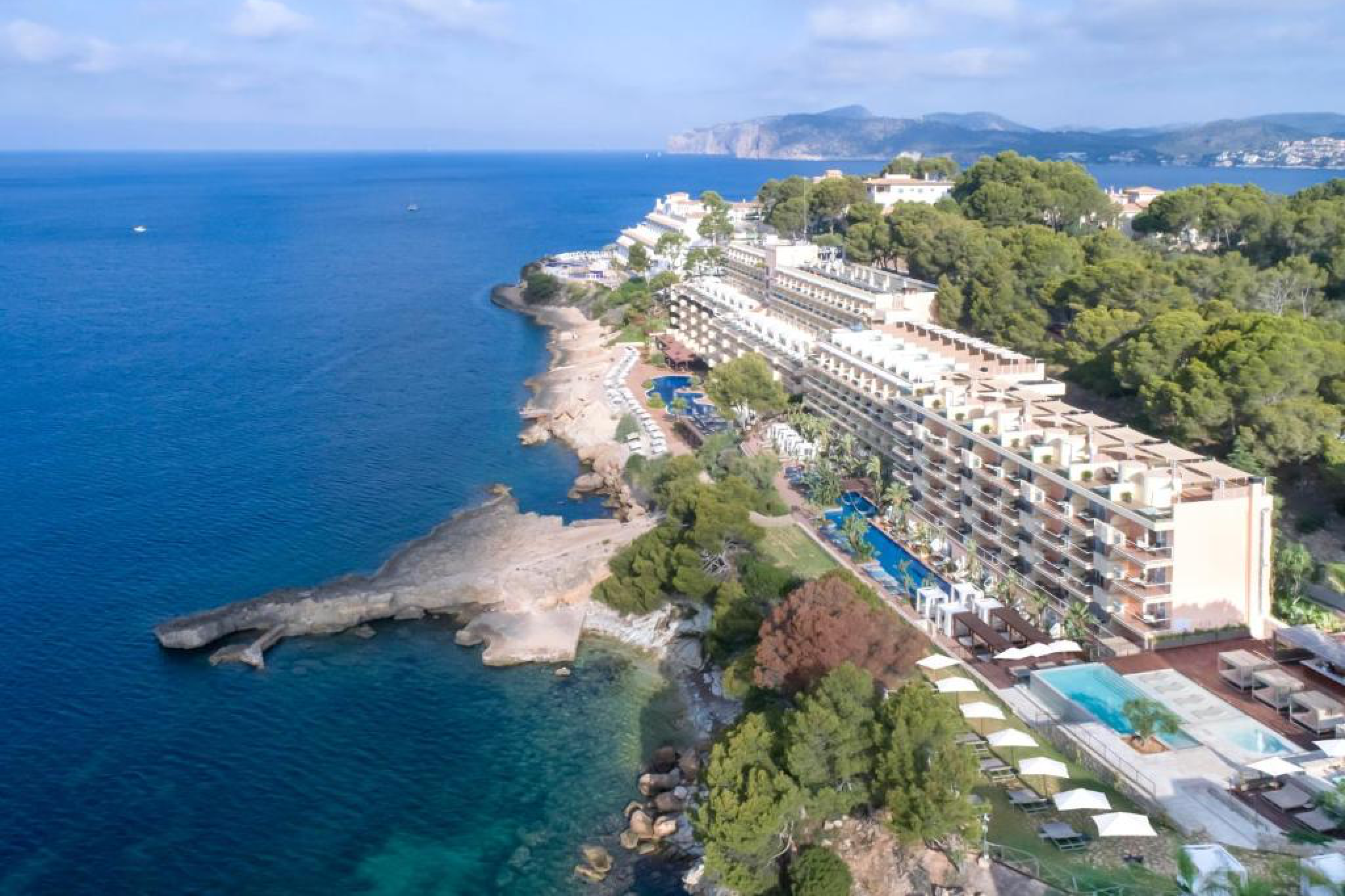 Aerial view of Iberostar Selection Jardín del Sol Suites perched on a rocky coastline in Mallorca, surrounded by pine trees and overlooking the calm turquoise Mediterranean — a serene adults-only retreat counted among the best beach resorts in Spain.