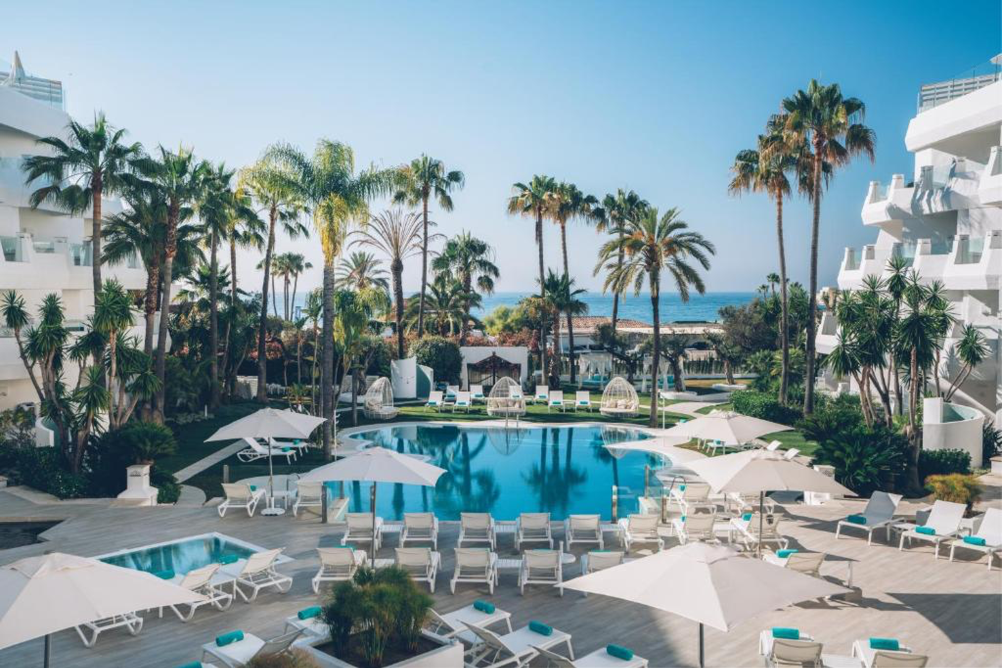 Daytime view of Iberostar Selection Marbella Coral Beach with chic white architecture, lush gardens, and a tranquil pool framed by tall palms overlooking the Mediterranean — a standout choice in the best beach resorts in Spain.