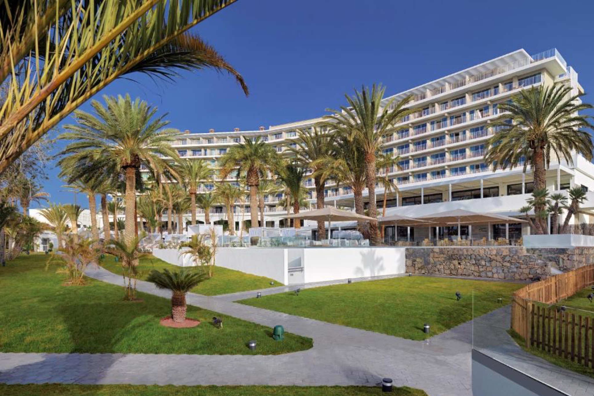 Expansive beachfront view of Paradisus Gran Canaria framed by palm trees, with contemporary terraces, manicured gardens, and direct access to golden sands — a top-rated all-inclusive retreat leading the list of the best beach resorts in Spain.