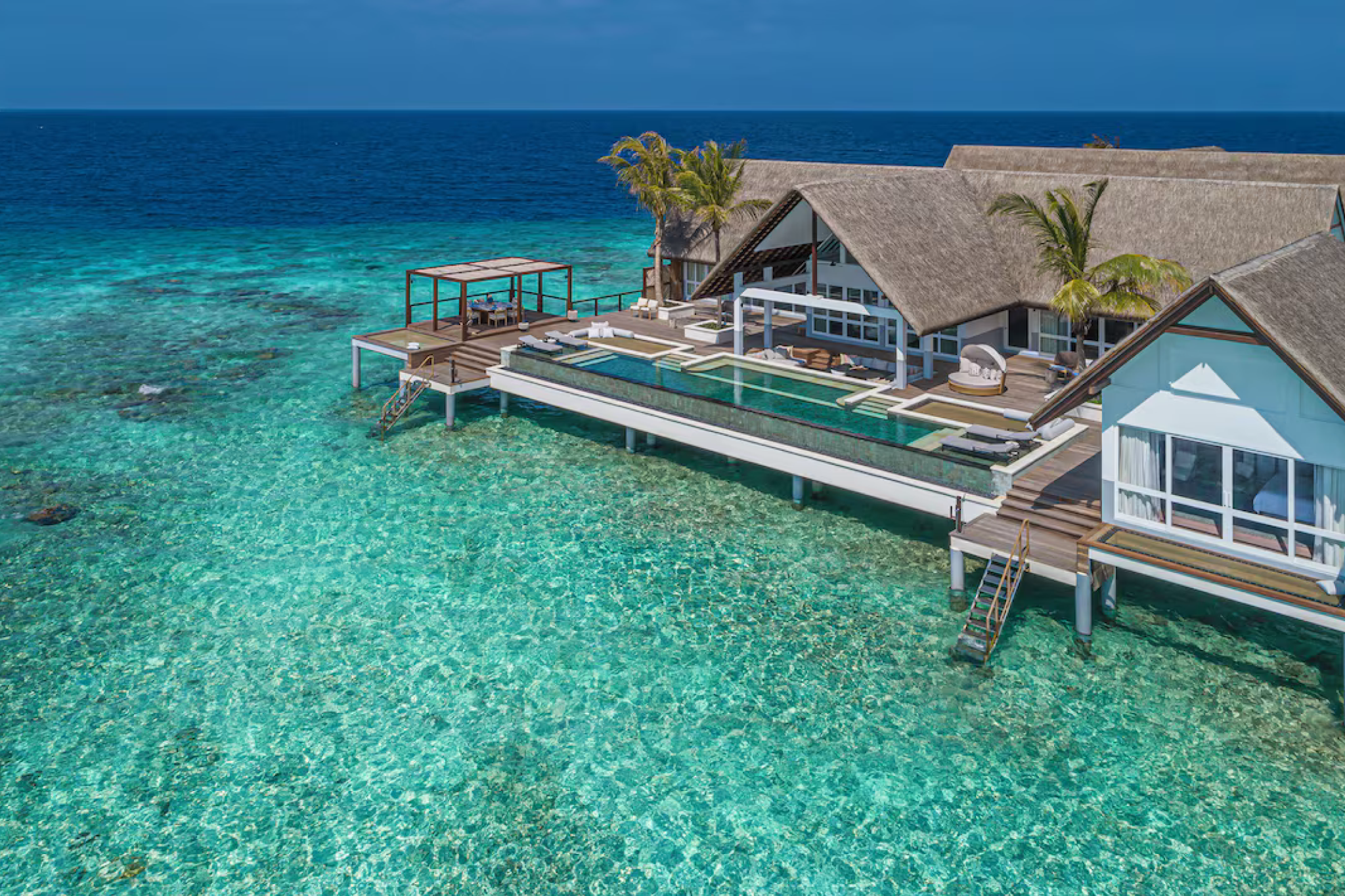 Overwater structures at Four Seasons Landaa Giraavaru rising above a clear reef lagoon, with the deep ocean beyond, showcasing the resort’s refined marine setting and its place among the best beach resorts in the Indian Ocean in 2025.