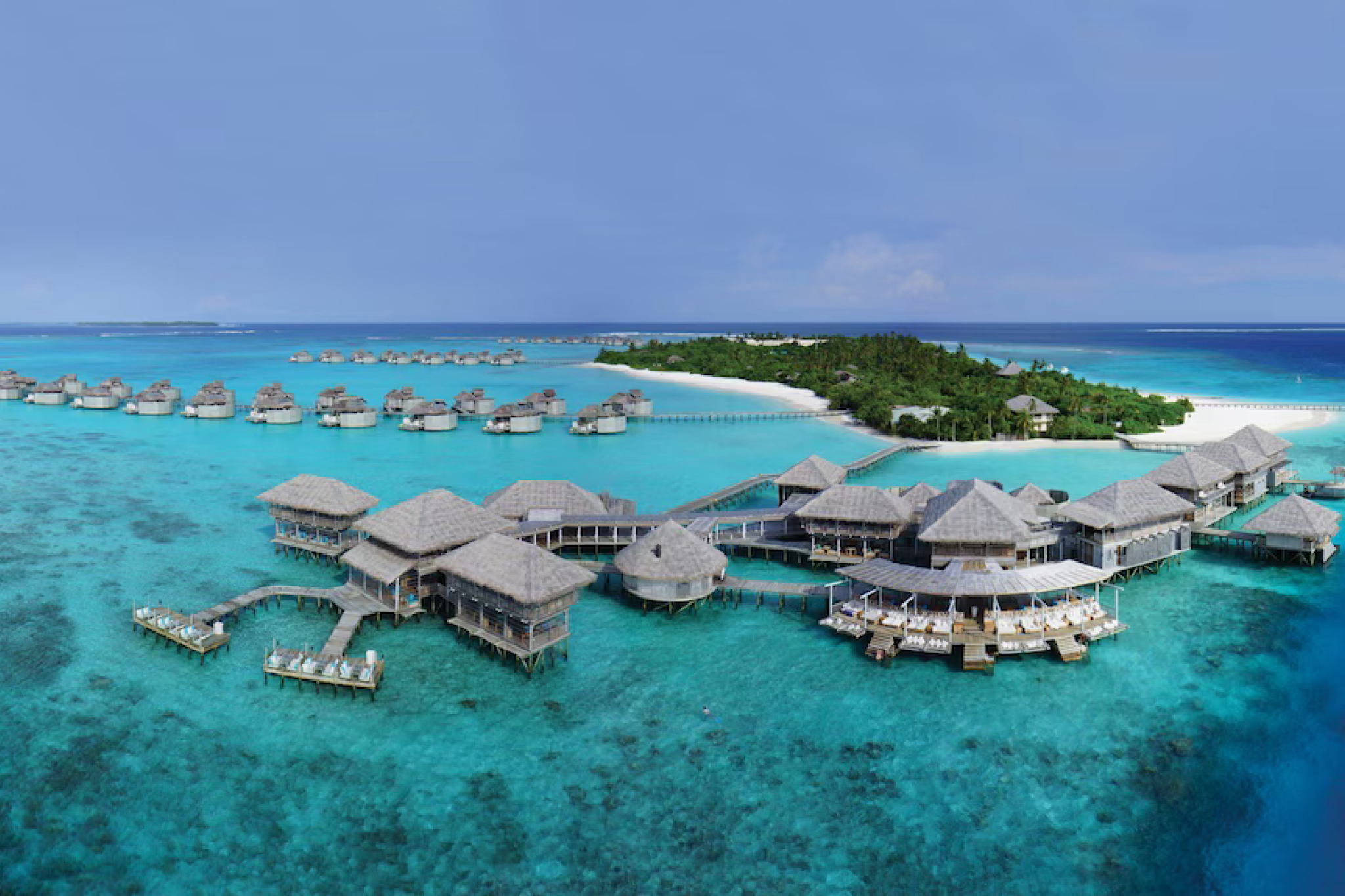 Expansive aerial view of Six Senses Laamu’s overwater villas and central lagoon surrounded by bright blue Maldivian waters, highlighting the resort’s eco-luxury environment as one of the best beach resorts in the Indian Ocean in 2025.