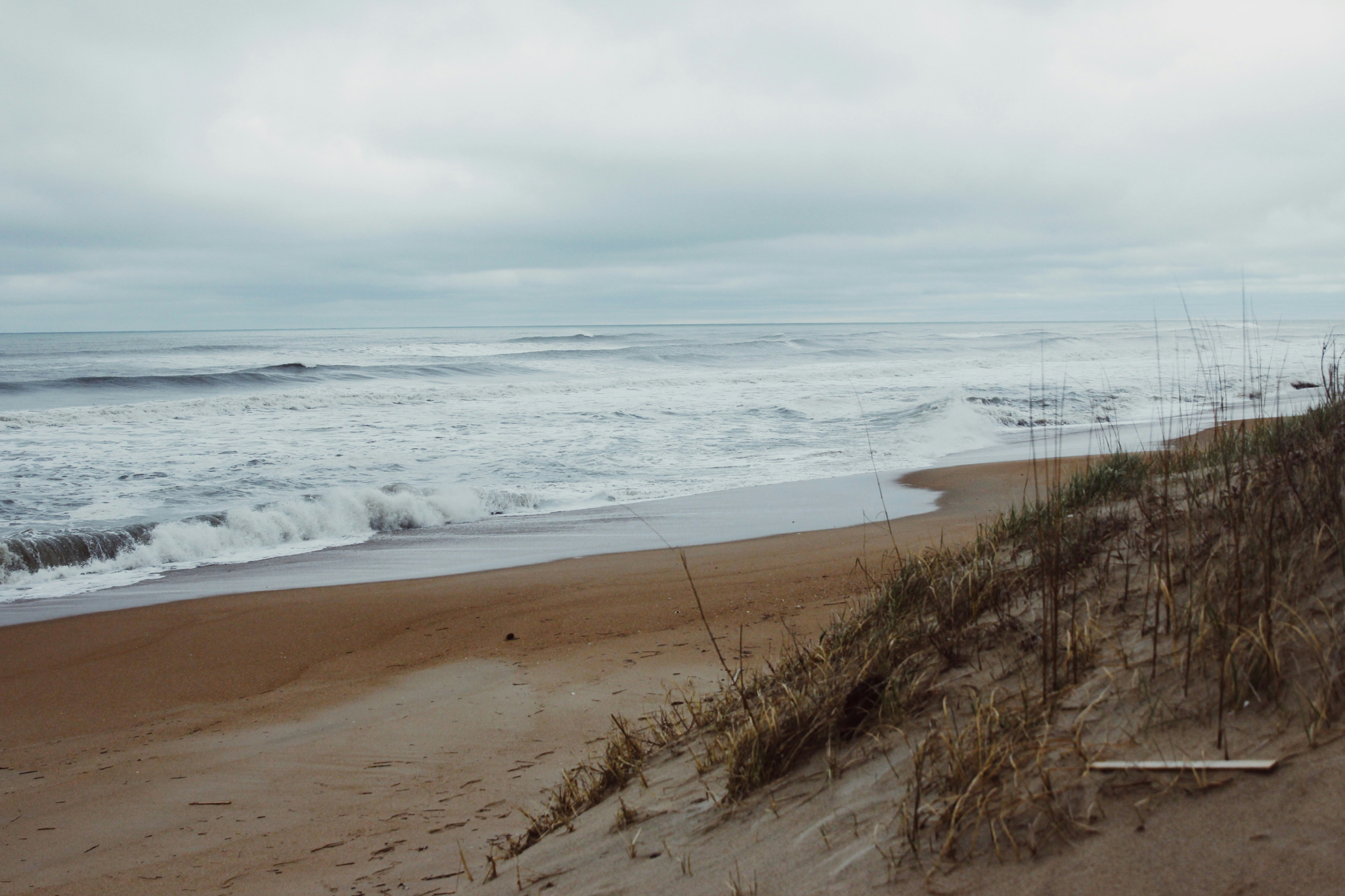 Untouched Corolla Beach Outer Banks shoreline with natural dune grasses and rolling waves, capturing the remote charm of one of the best beaches on the US East Coast