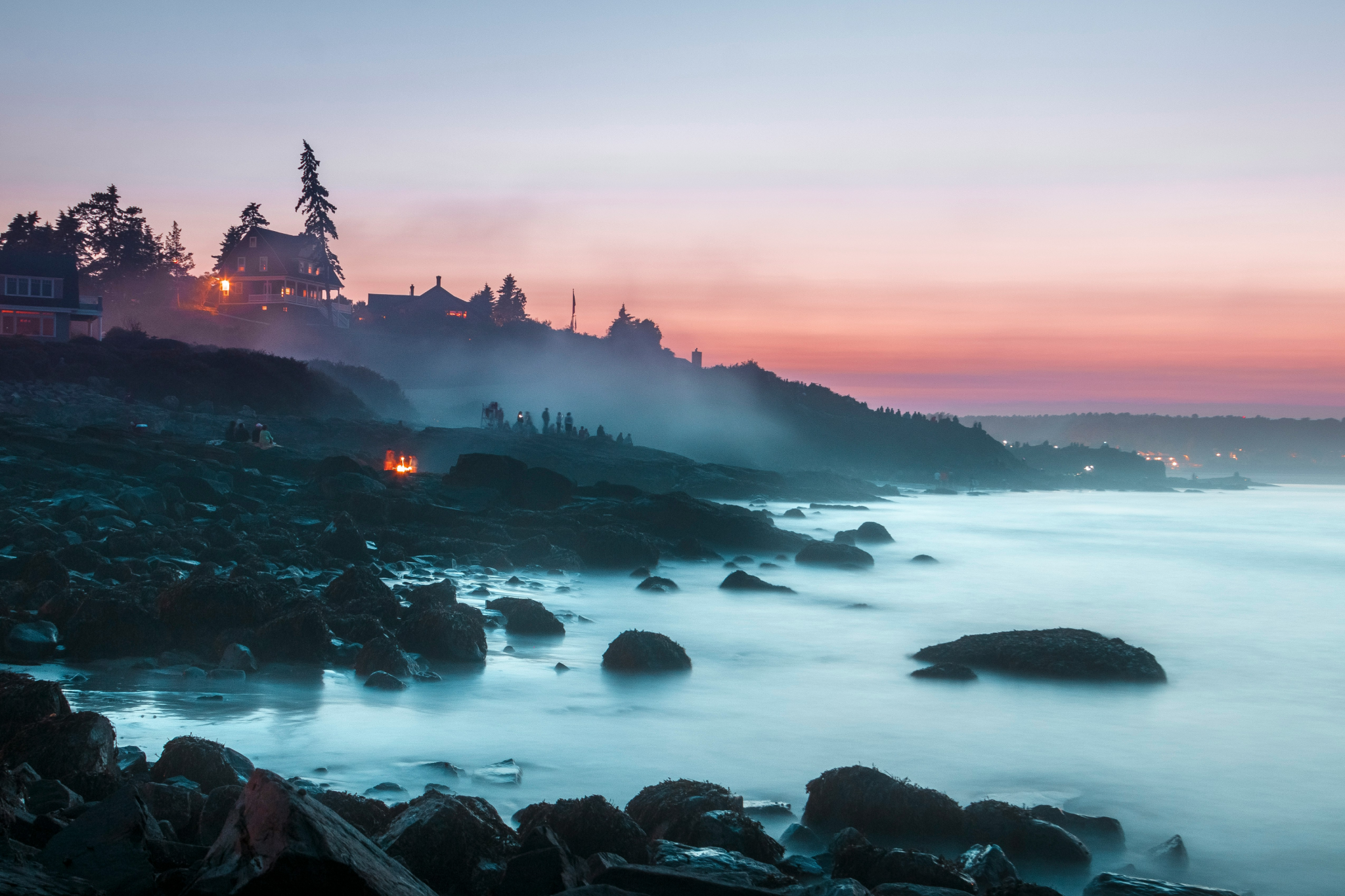 Dramatic sunset over rocky Maine coastline with illuminated coastal homes, showcasing why Ogunquit Beach ranks among the best beaches on the US East Coast