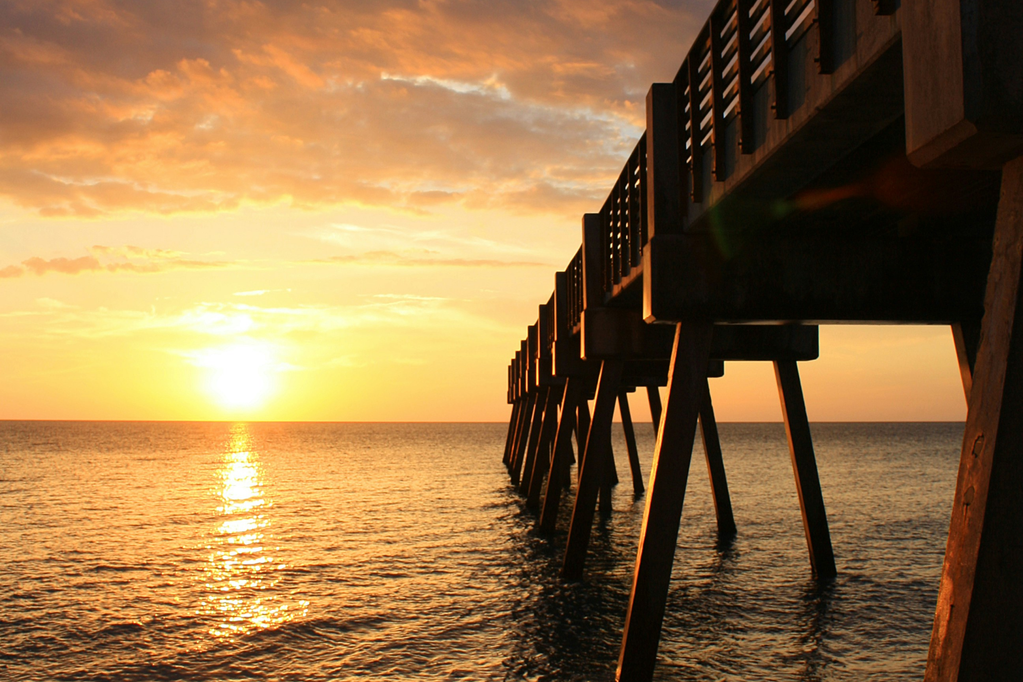 Golden sunset over wooden fishing pier at Vero Beach Florida with dramatic orange sky reflecting on calm Atlantic waters, completing the collection of the best beaches on the US East Coast