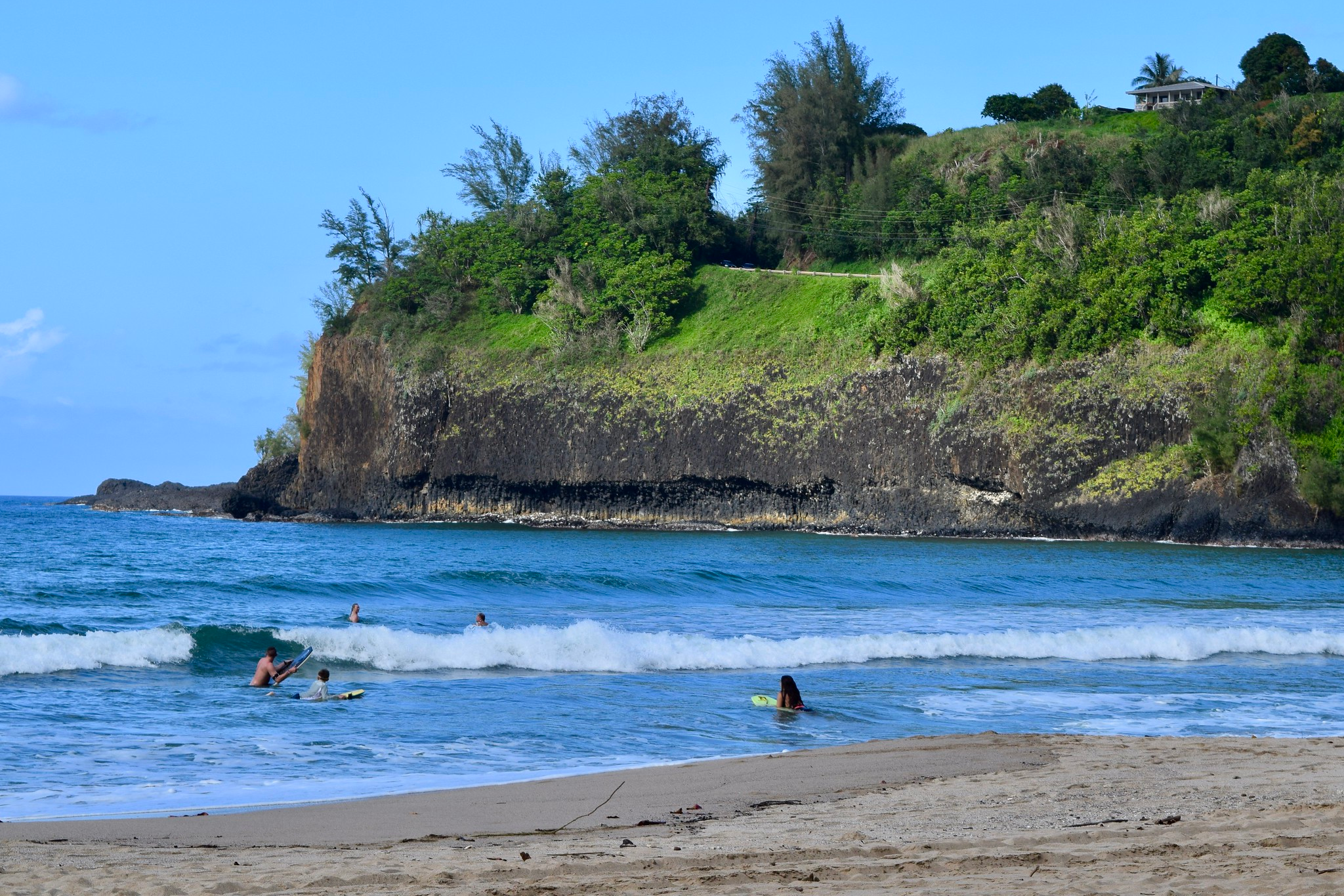 Bodyboarders ride waves at Shipwreck’s Beach, backed by lava cliffs and greenery—one of the best beaches in Kauai for adventure and coastal hiking.
