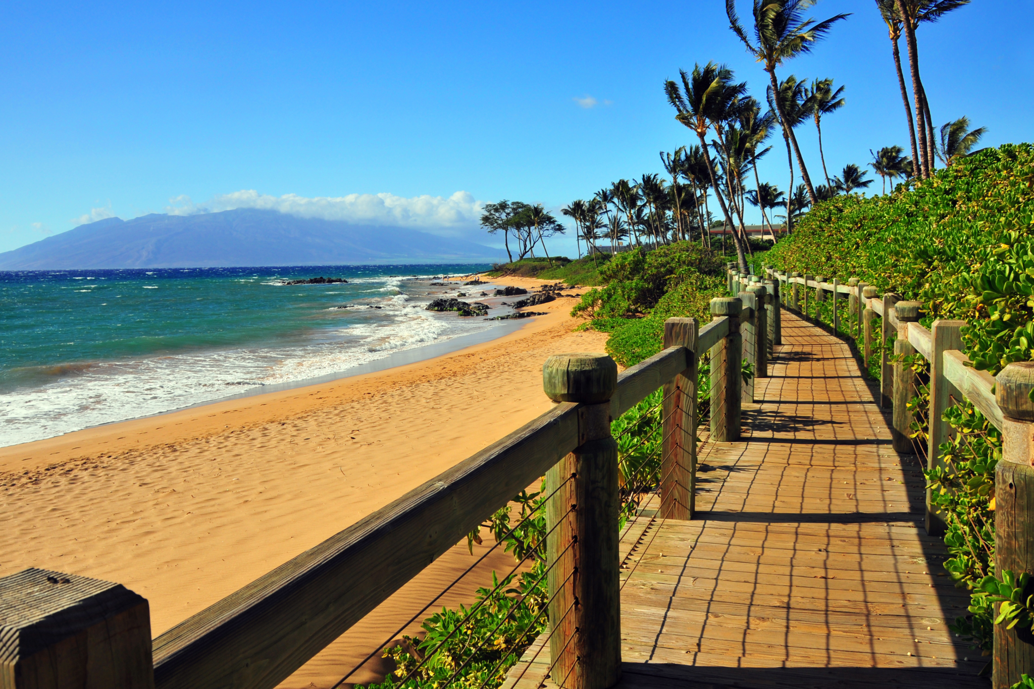 Sunlit wooden boardwalk overlooking Wailea Beach with soft sand and tall palms, a top choice among the best beaches in Maui for refined relaxation.