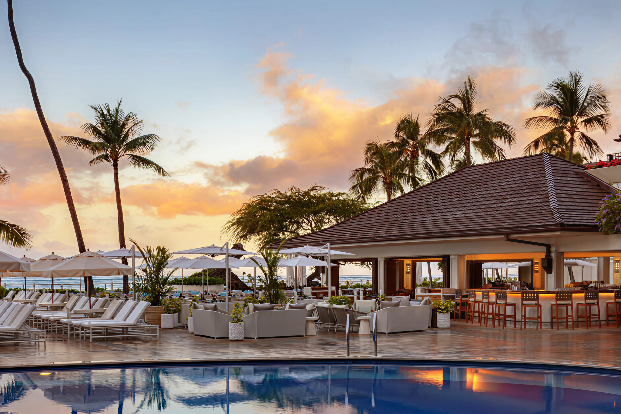 Halepuna Waikiki boutique hotel pool deck at sunset with modern lounge seating and tropical palms, intimate best beachfront hotels in Waikiki