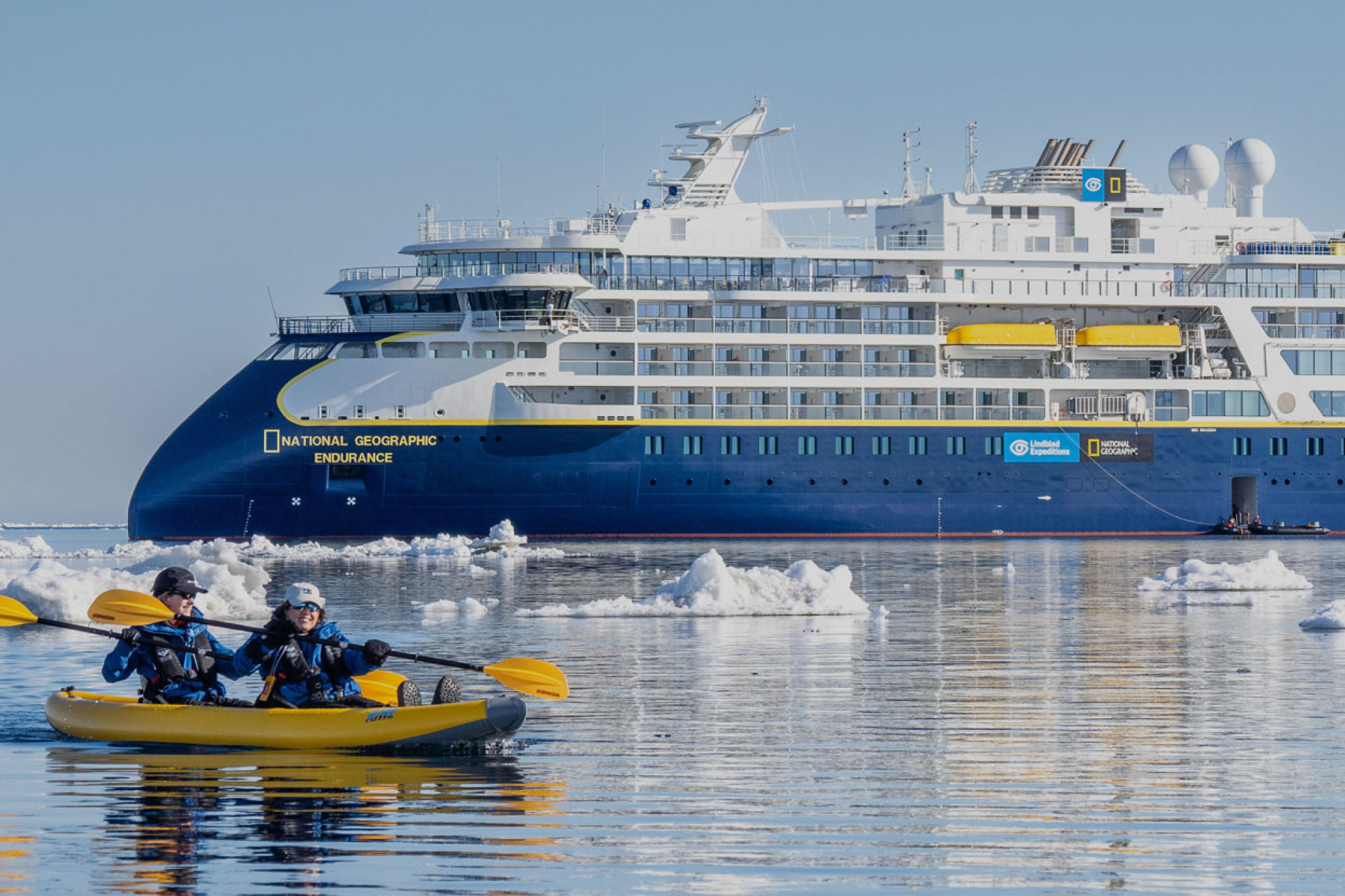 National Geographic Endurance ship in icy polar waters with kayakers nearby, capturing the spirit of exploration that defines these voyages — among the Best Cruises for Honeymoon travelers who crave adventure and discovery.