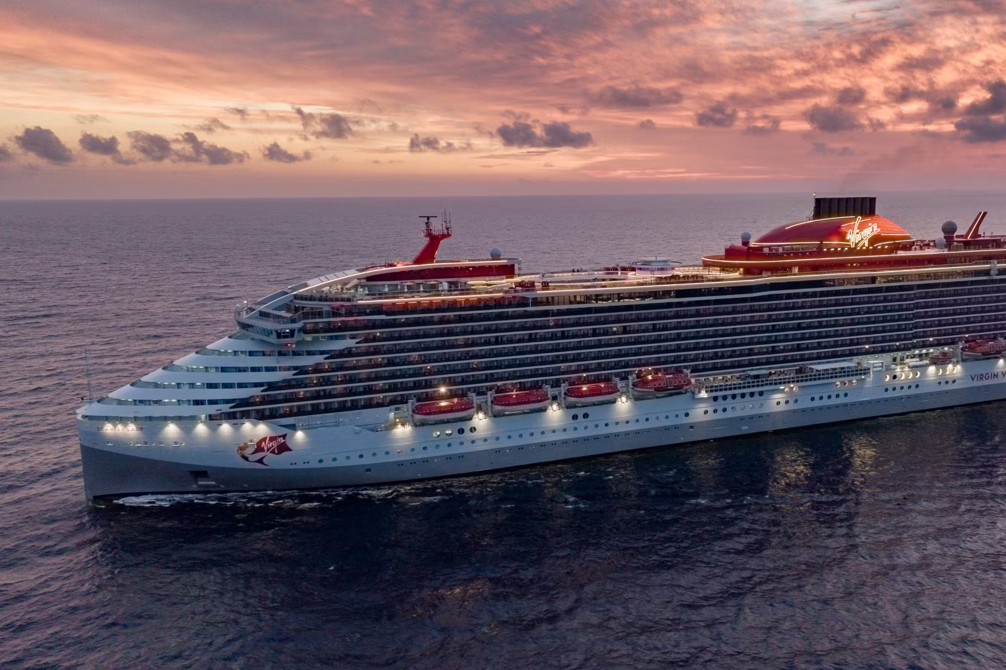 Virgin Voyages cruise ship illuminated at sunset — one of the best cruises for partying with upscale, adults-only nightlife and stylish ocean vibes.