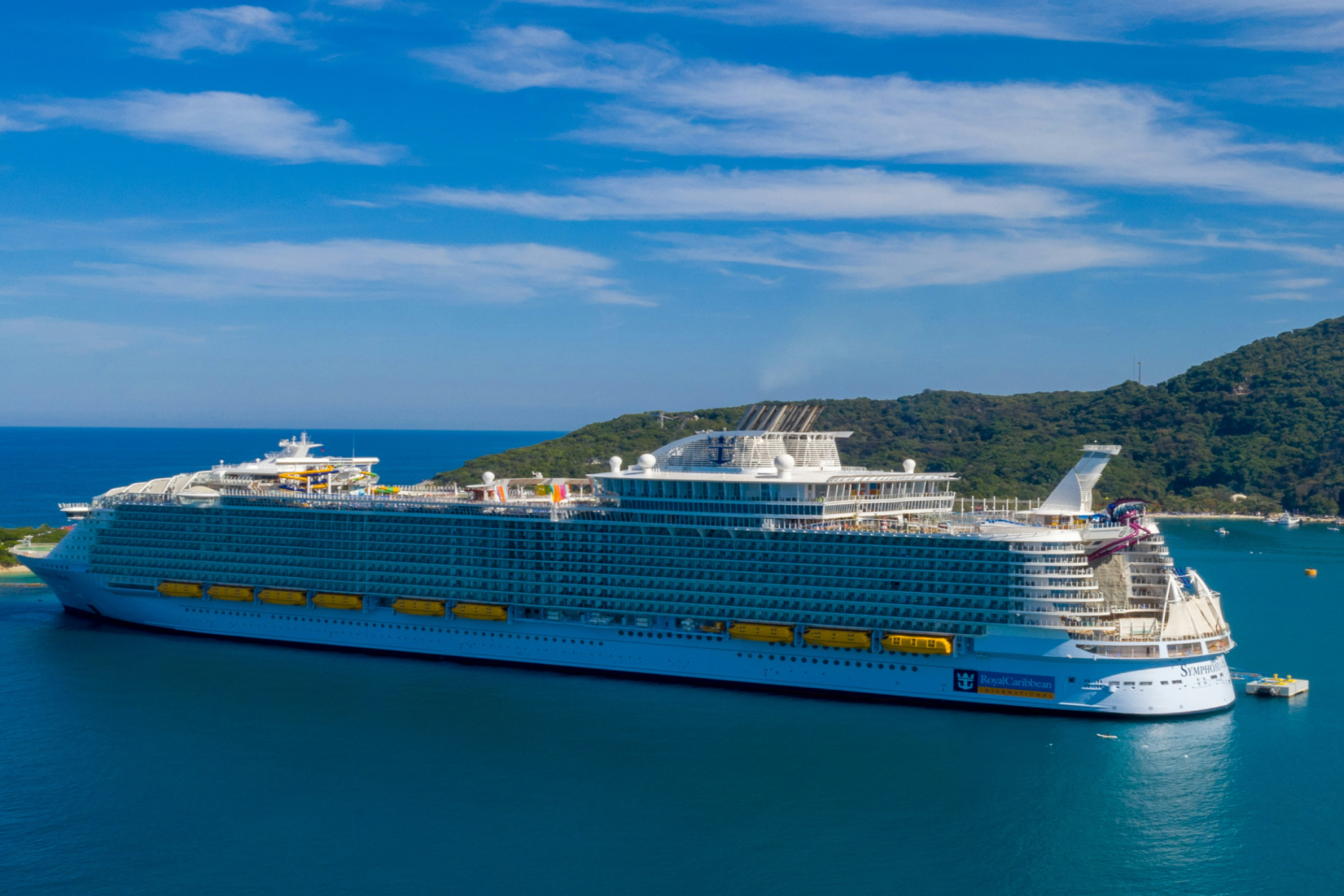 Royal Caribbean Symphony of the Seas docked near an island, representing the best cruises for teens thanks to surf simulators, climbing walls, and teen-only lounges.