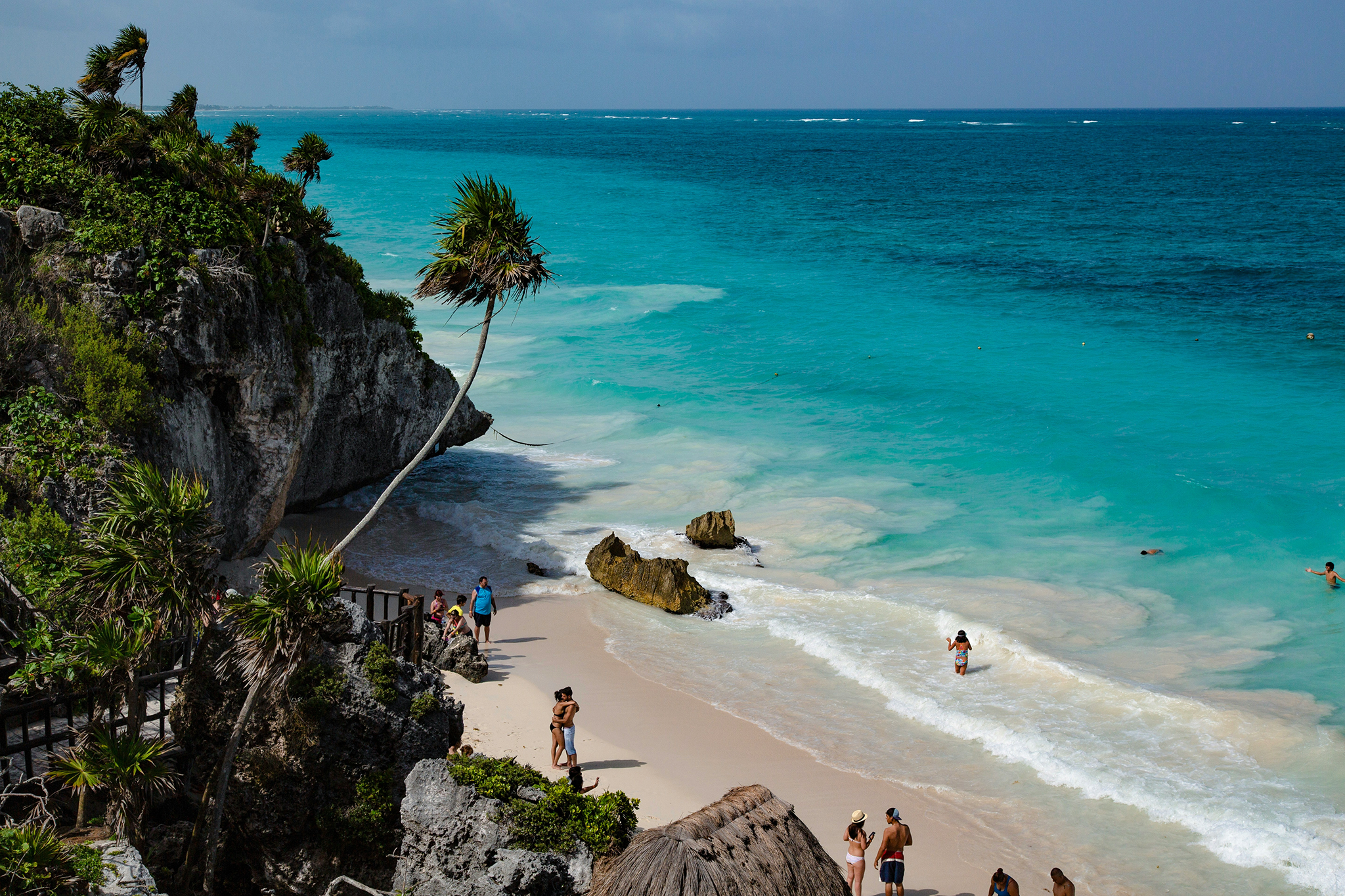 A scenic cove below ancient cliffs in Tulum, Mexico, with turquoise waters and beachgoers enjoying the sunshine — a cultural and eco-luxury hub among the best destinations for Christmas on the beach.