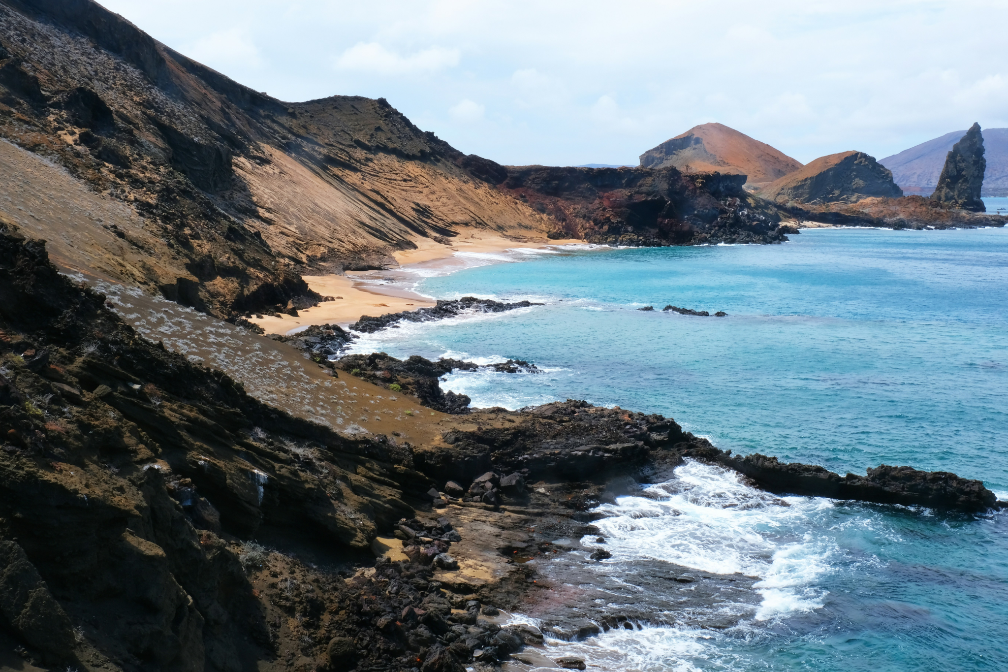 Dramatic volcanic coastline of the Galápagos Islands with rugged black rock formations, untouched golden sand coves, and turquoise water breaking against the shore — a defining landscape of the best islands in the world in 2025.