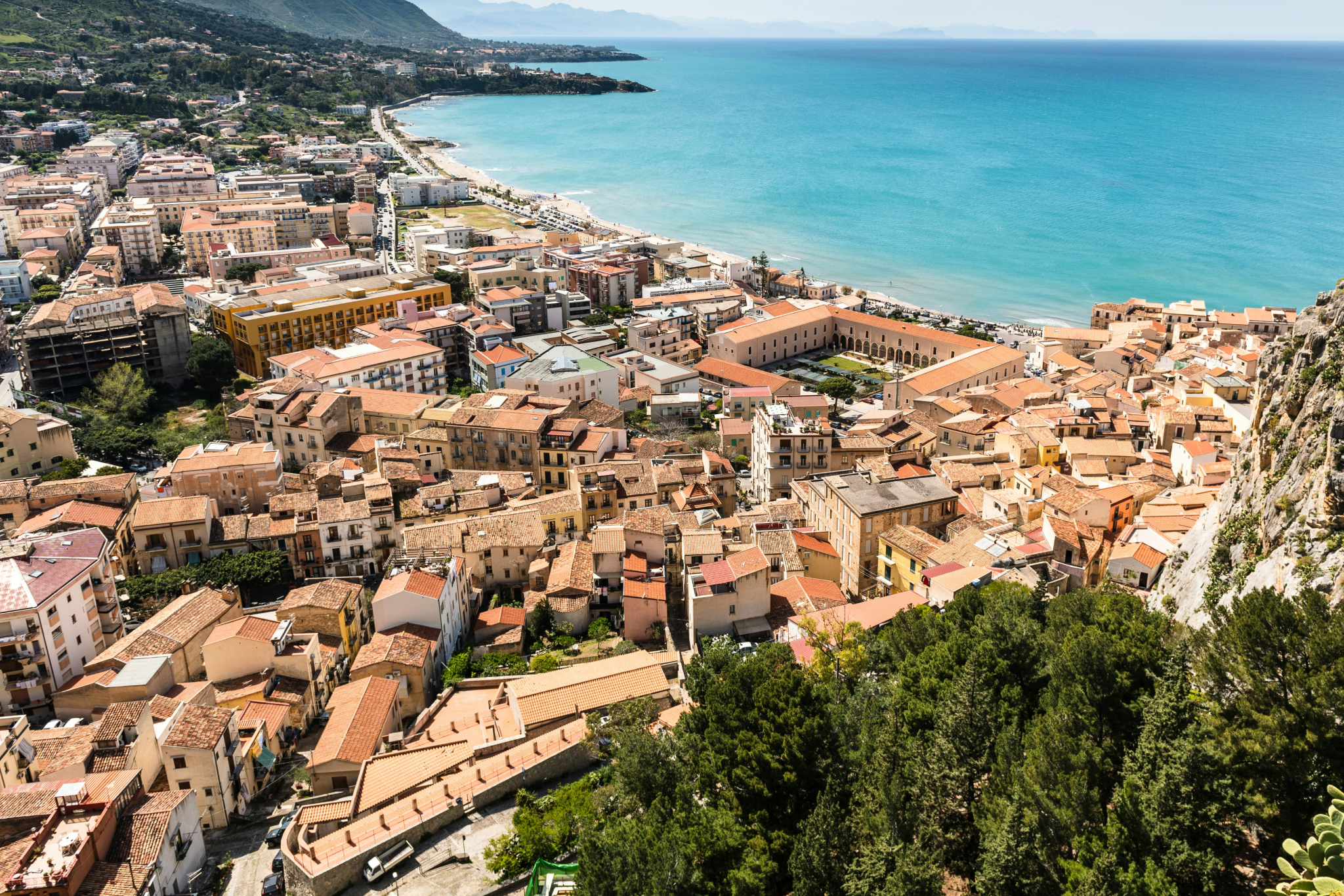 Expansive coastal view of Sicily featuring historic terracotta-roofed towns, rugged mountainous terrain, and bright blue Mediterranean waters stretching along the shoreline — a vivid portrait of one of the best islands in the world in 2025.