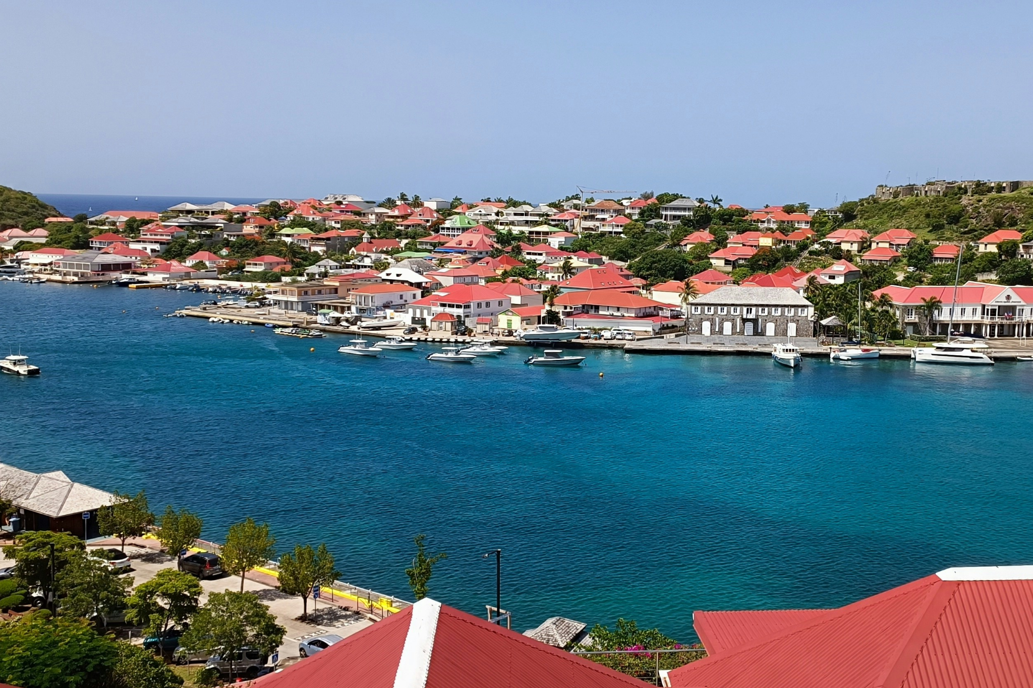 Aerial view of St. Barts’ Gustavia harbor with red-roofed villas, calm turquoise water, anchored yachts, and a refined Caribbean village atmosphere — showcasing why St. Barts ranks among the best islands in the world in 2025.