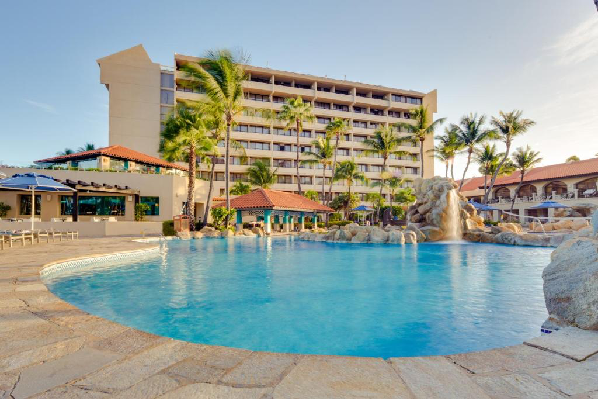 Barceló Aruba, among the best resorts in Aruba, showcasing its expansive pool, swim-up bar, and oceanfront rooms framed by palm trees on Palm Beach.