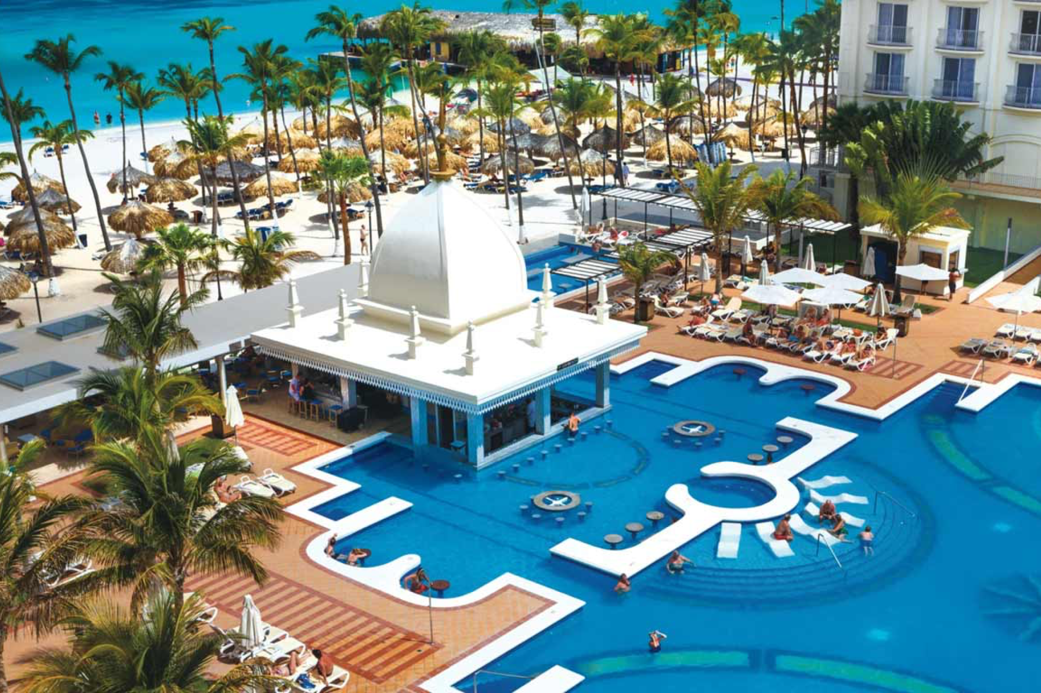 Hotel Riu Palace Aruba, top-ranked among the best resorts in Aruba, showcasing a grand pool complex, domed architecture, and beachfront elegance on Palm Beach.