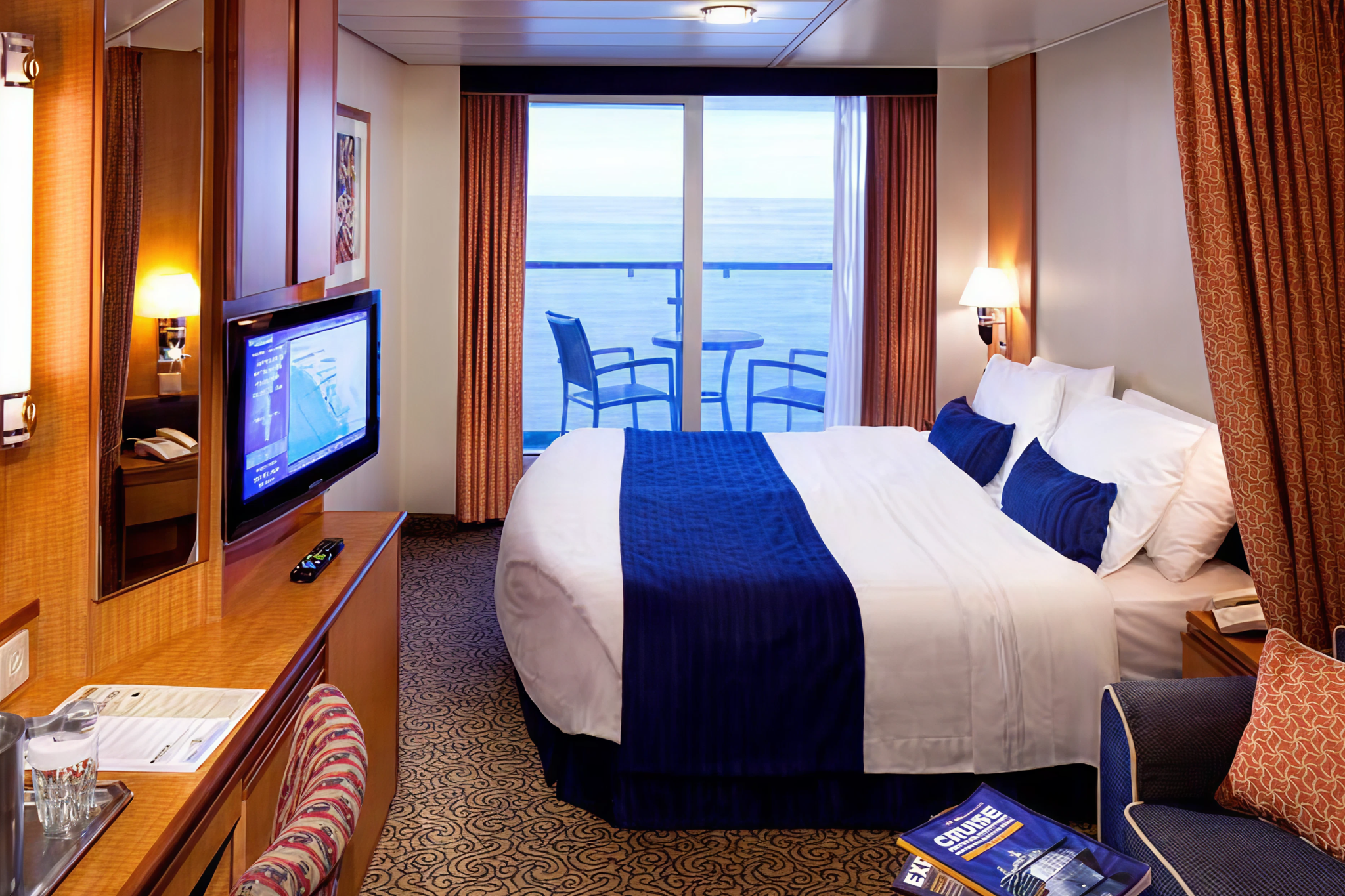 Balcony stateroom on Brilliance of the Seas featuring ocean views, a large bed with blue accents, and a private outdoor seating area.
