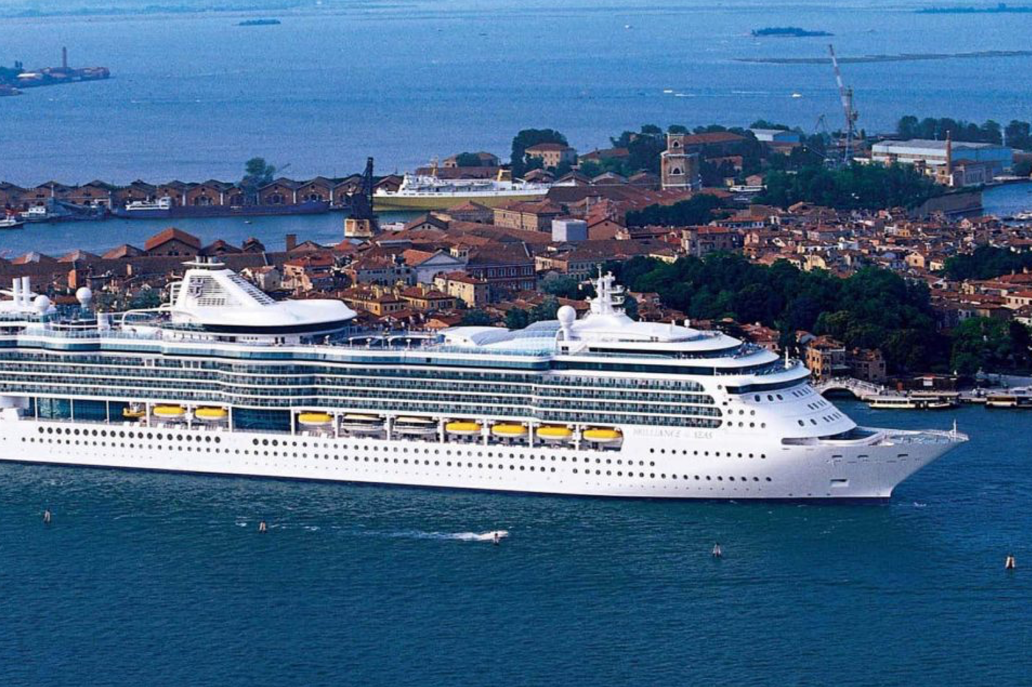Brilliance of the Seas docked near a historic European port, showcasing its sleek white hull and glass-walled decks.