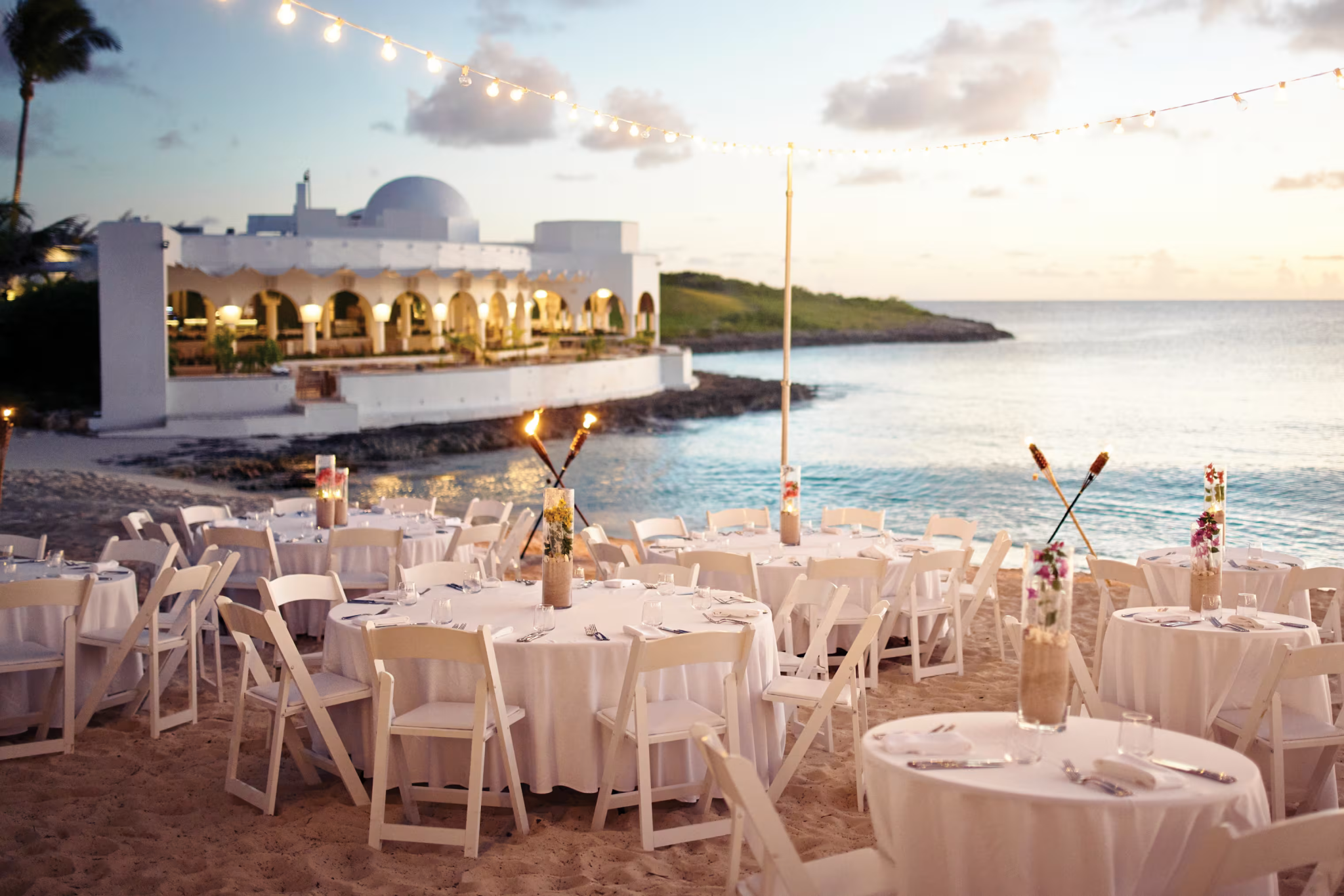 Evening event setup on the beach at Cap Juluca, featuring round tables, string lights, and the resort’s signature domed architecture in the background.