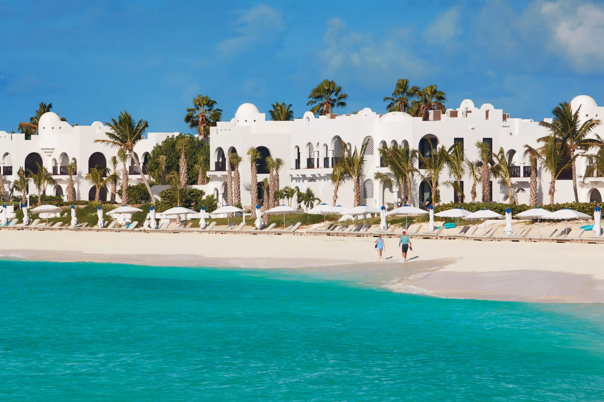 Whitewashed Greco-Moorish villas of Cap Juluca, A Belmond Hotel, stretch along Maundays Bay with turquoise waters and private beach loungers in view.