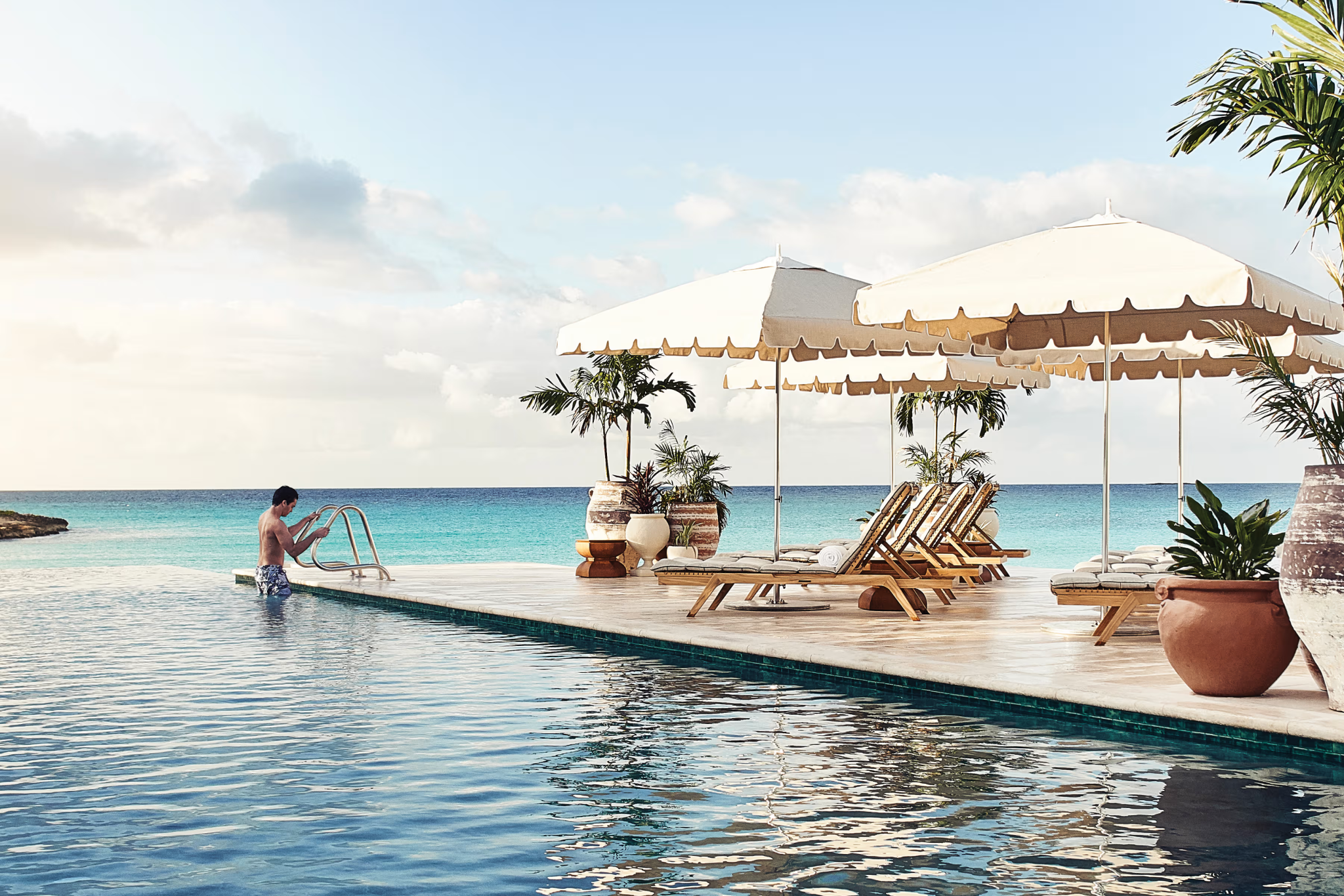 Infinity pool at Cap Juluca, A Belmond Hotel, framed by cream parasols, terracotta planters, and views of the calm Caribbean Sea beyond.