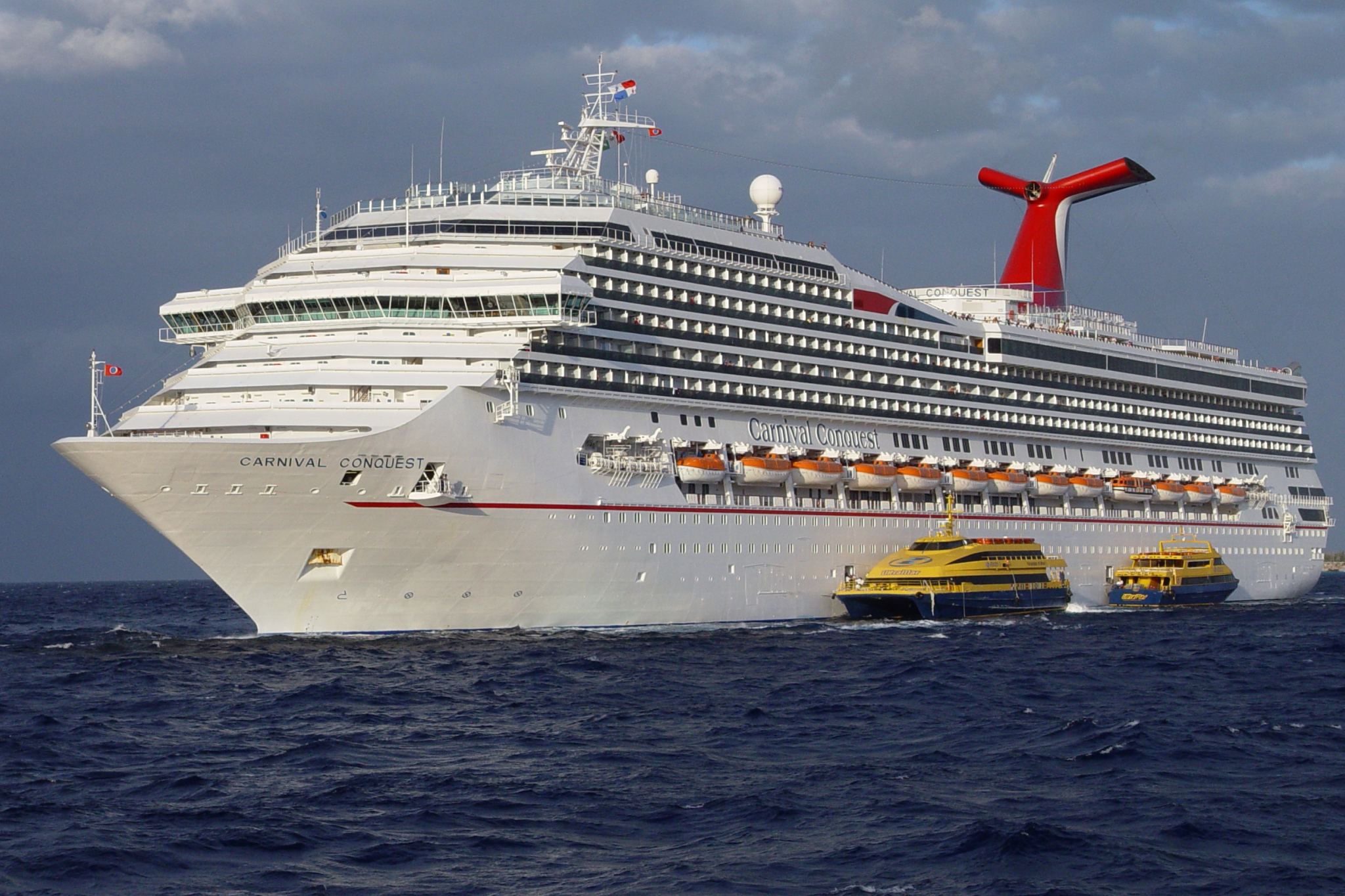 Carnival Cruise Lines Ships by Size reference image of Carnival Conquest underway, with its broad mid-sized hull, continuous balcony rows, and expansive top deck