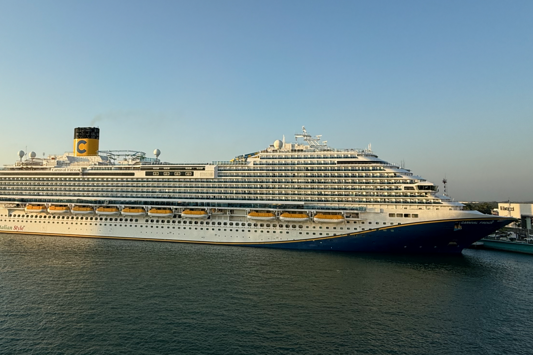 Carnival Firenze cruise ship docked at port in daylight, showing multiple decks, balcony cabins, and the signature blue-and-gold hull design.
