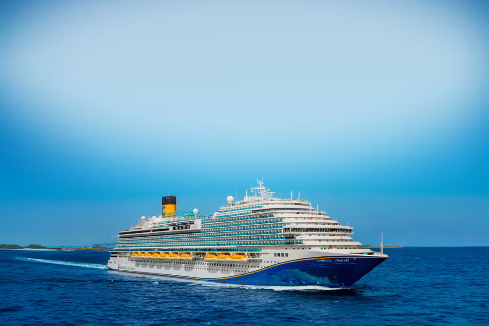 Carnival Venezia cruise ship sailing at sea with its signature blue hull and yellow lifeboats.