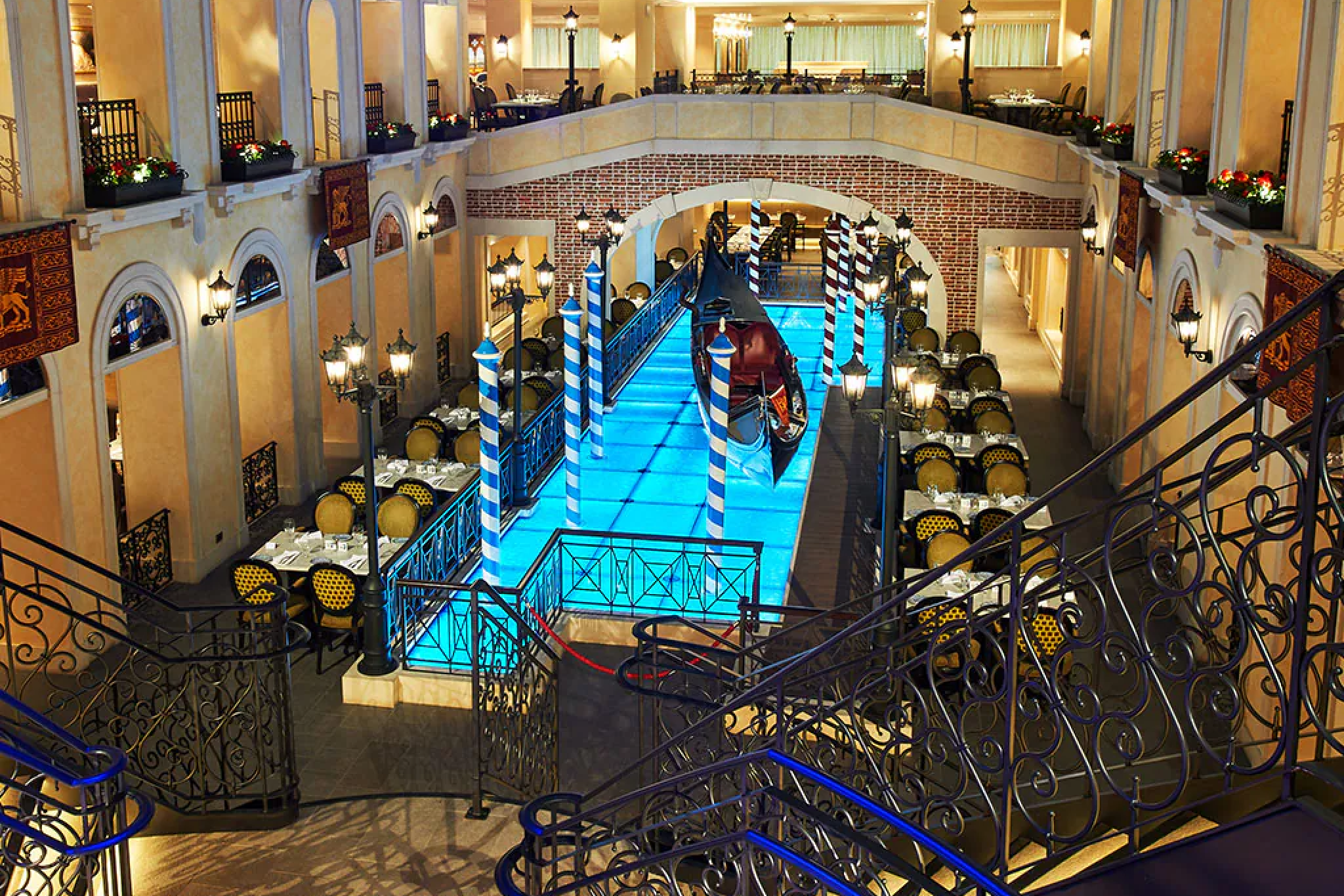 Venetian-inspired atrium on Carnival Venezia featuring gondola, blue-lit canal, and ornate dining areas.