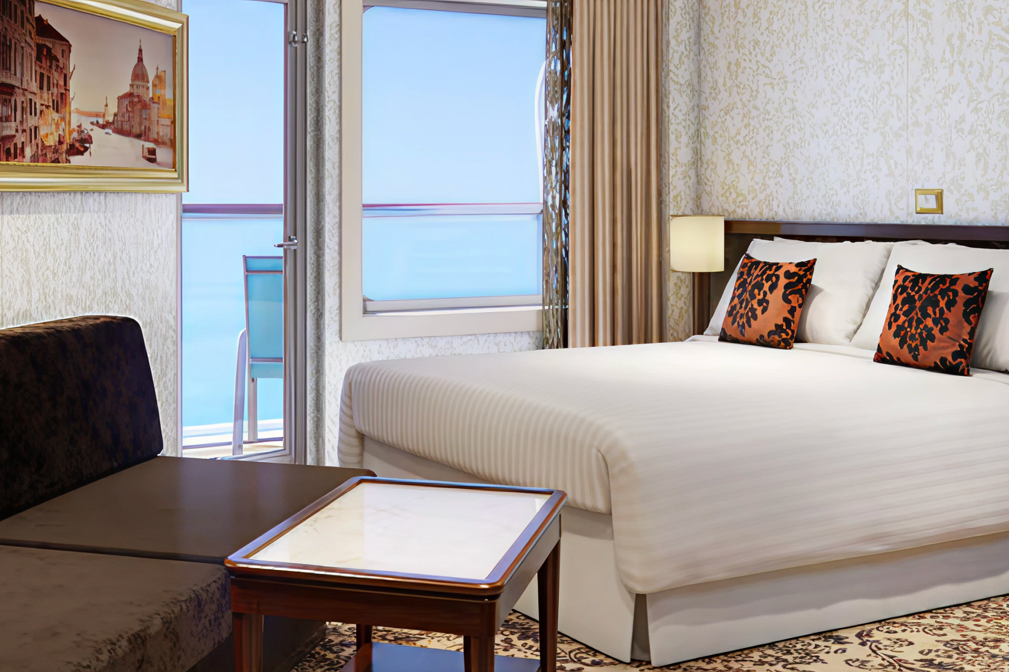 Carnival Venezia balcony stateroom featuring a double bed, sitting area, and ocean views.