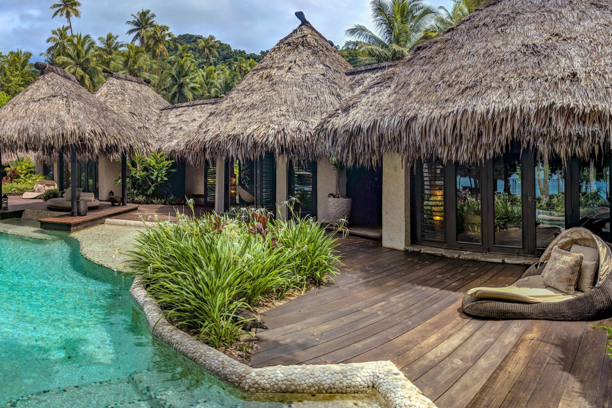 Private villa with traditional thatched roofs and lush landscaping beside a freeform pool at COMO Laucala Island.