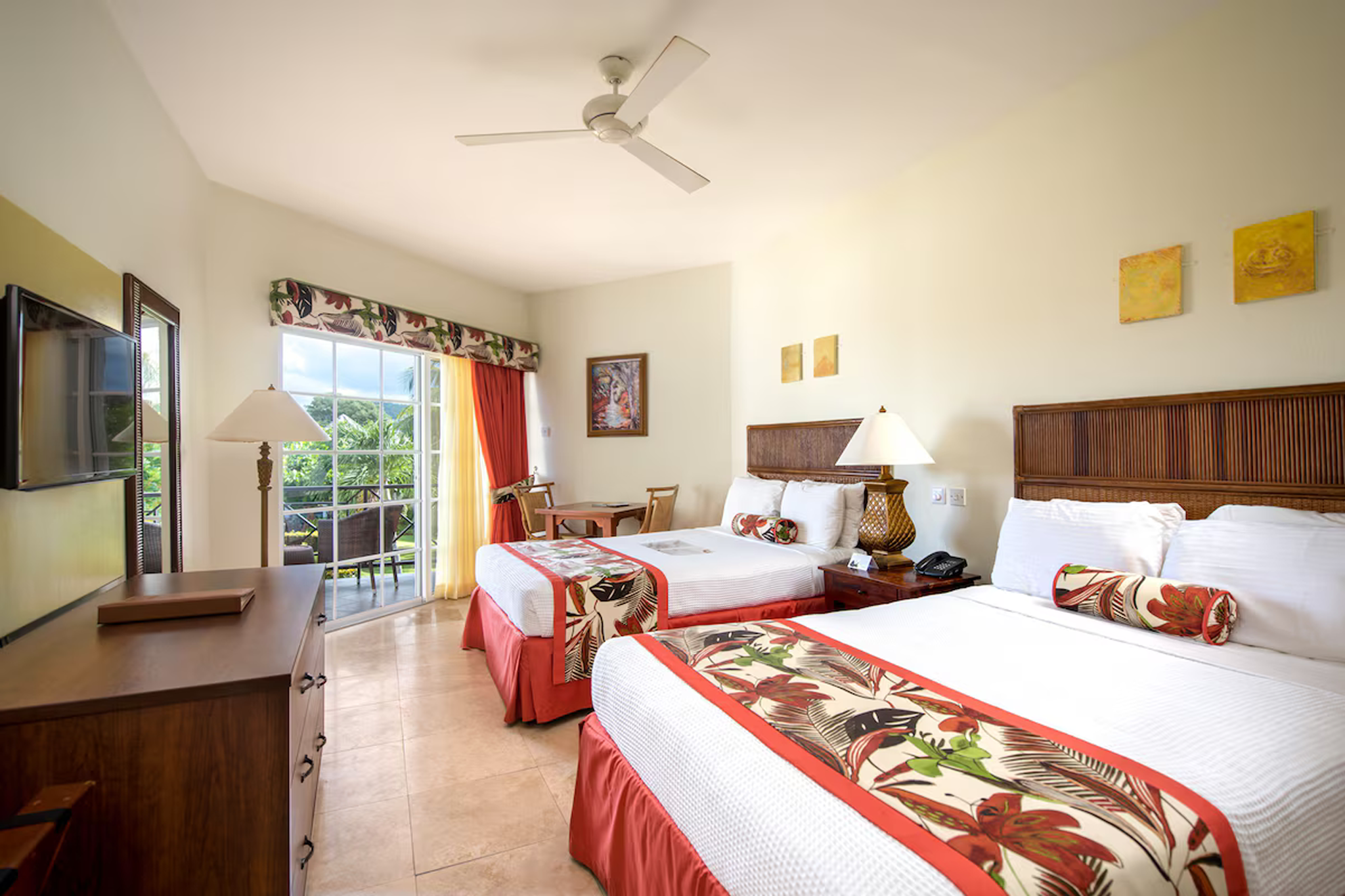 Spacious guest room at Coyaba Beach Resort featuring two queen beds, tropical decor, and a private balcony with garden views.