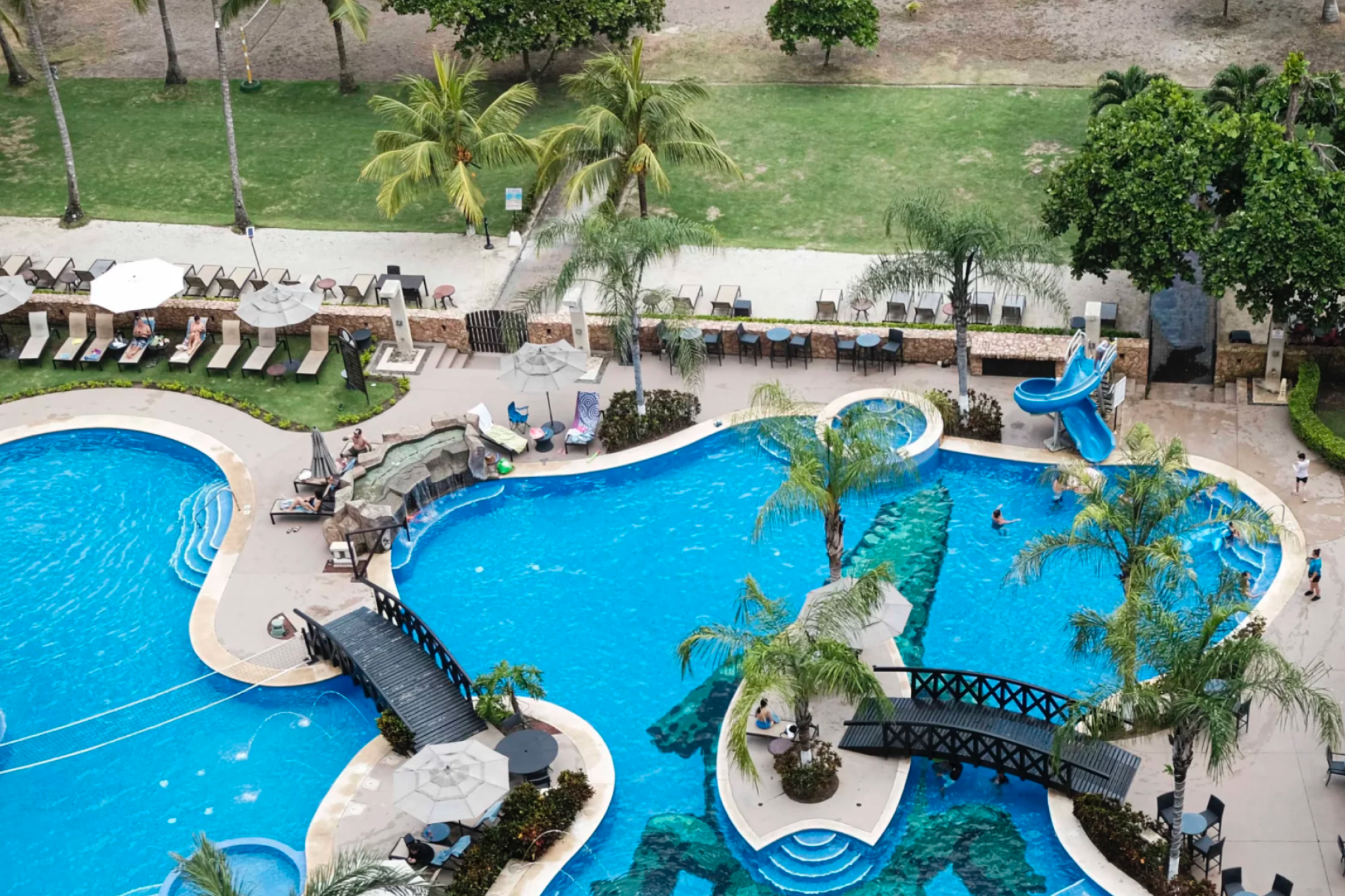 Aerial shot of Crocs Resort & Casino’s resort pool with bridges, swim-up bar, loungers, and a kids’ water slide near the beach.